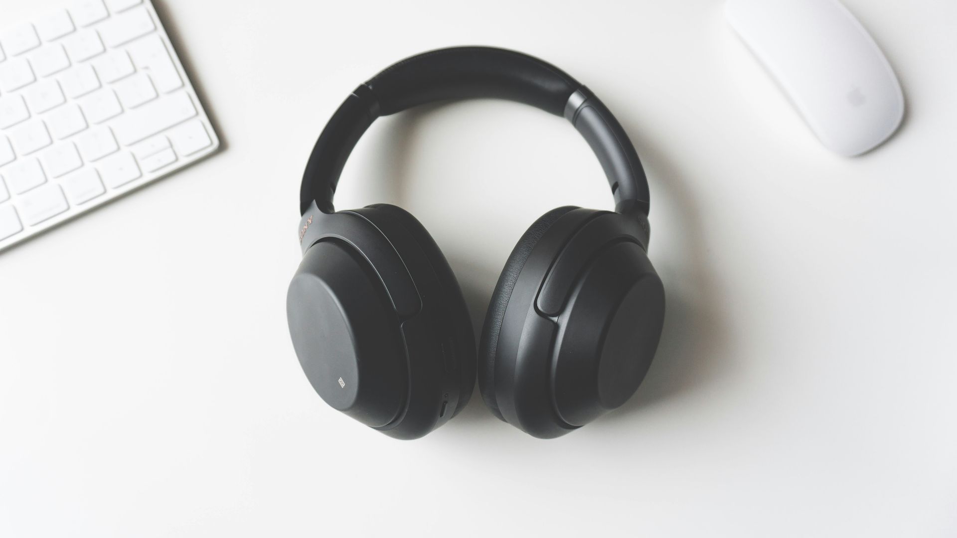 black wireless headphones between Apple Keyboard and Apple Magic Mouse on white surface