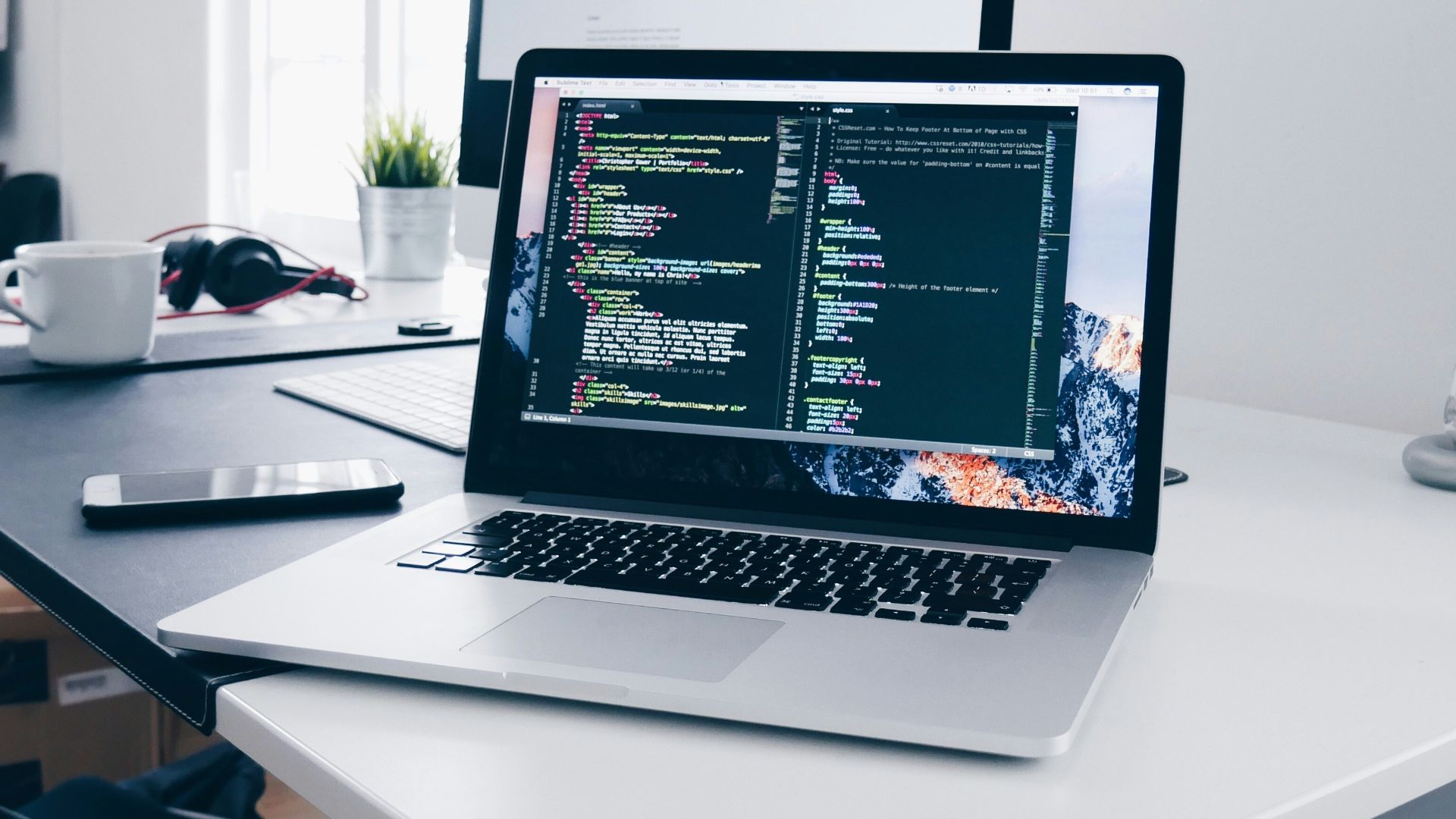A MacBook with lines of code on its screen on a busy desk