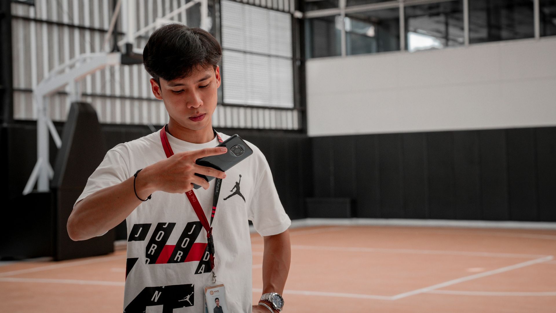 a young man standing on a basketball court holding a cell phone