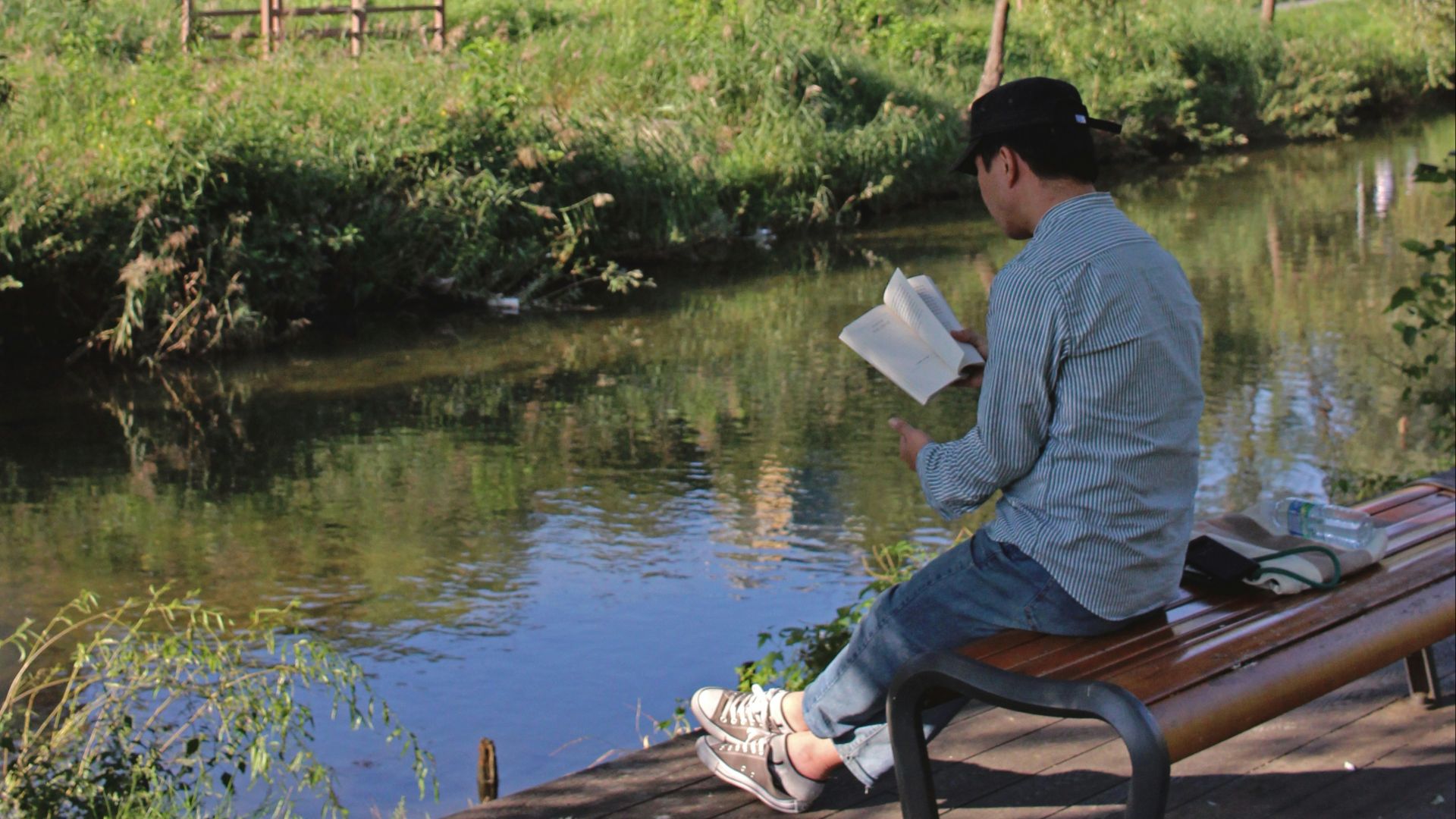 man reading book while sitting near body of water