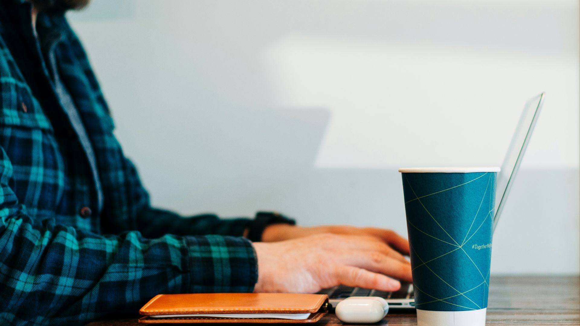man wearing blue and green plaid collared button-up long-sleeved shirt sitting while using laptop computer