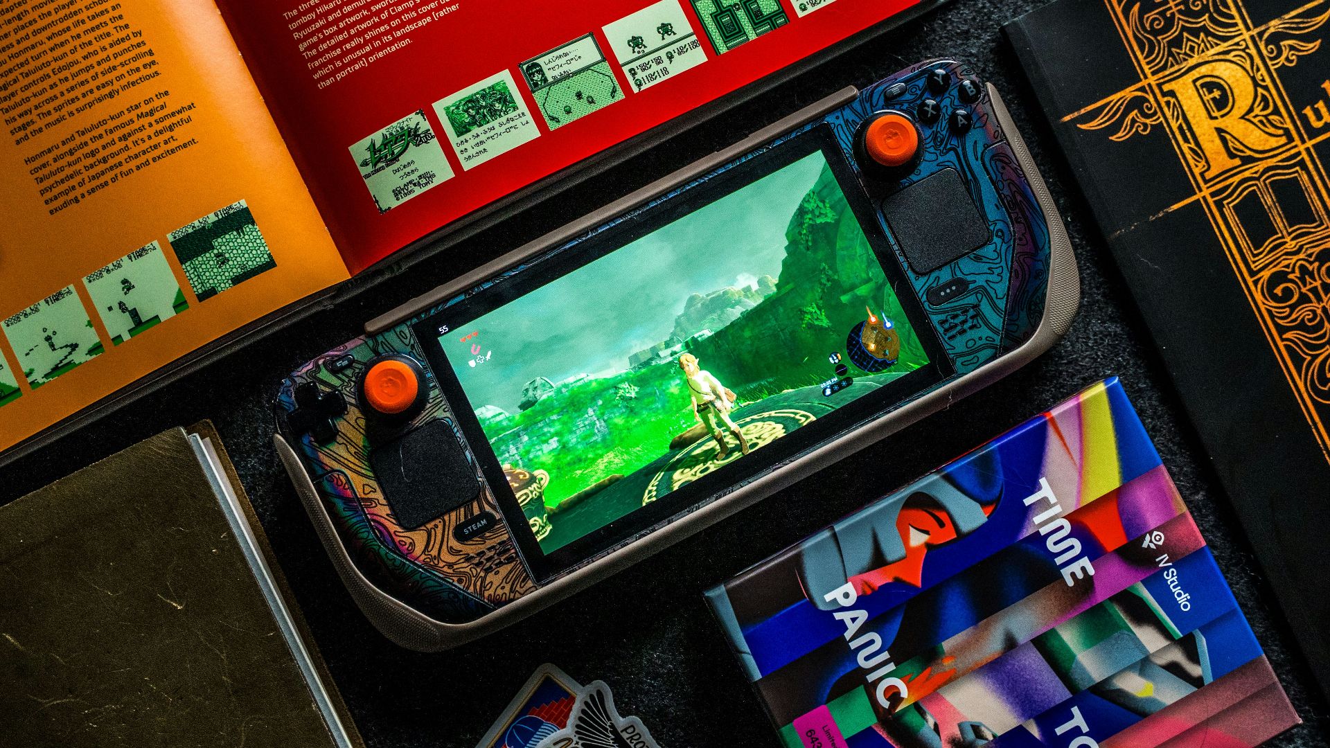 Gaming handheld, books, and phone on dark surface.