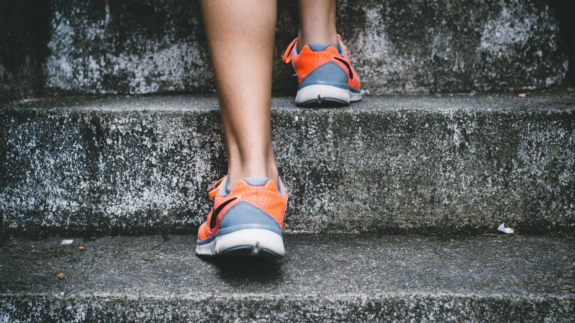 person wearing orange and gray Nike shoes walking on gray concrete stairs