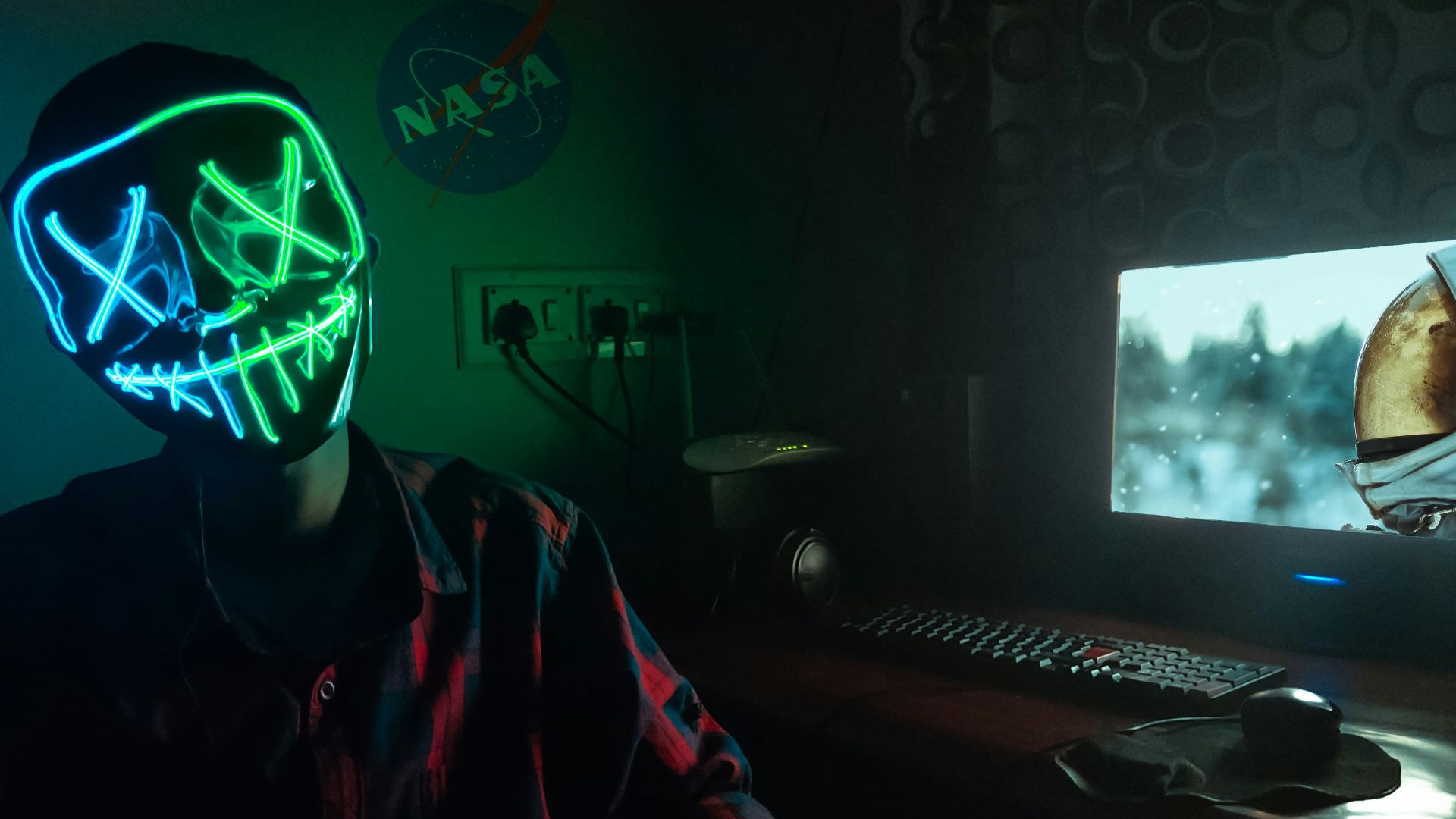person in blue and green LEd mask sitting in front of turned-on computer monitor
