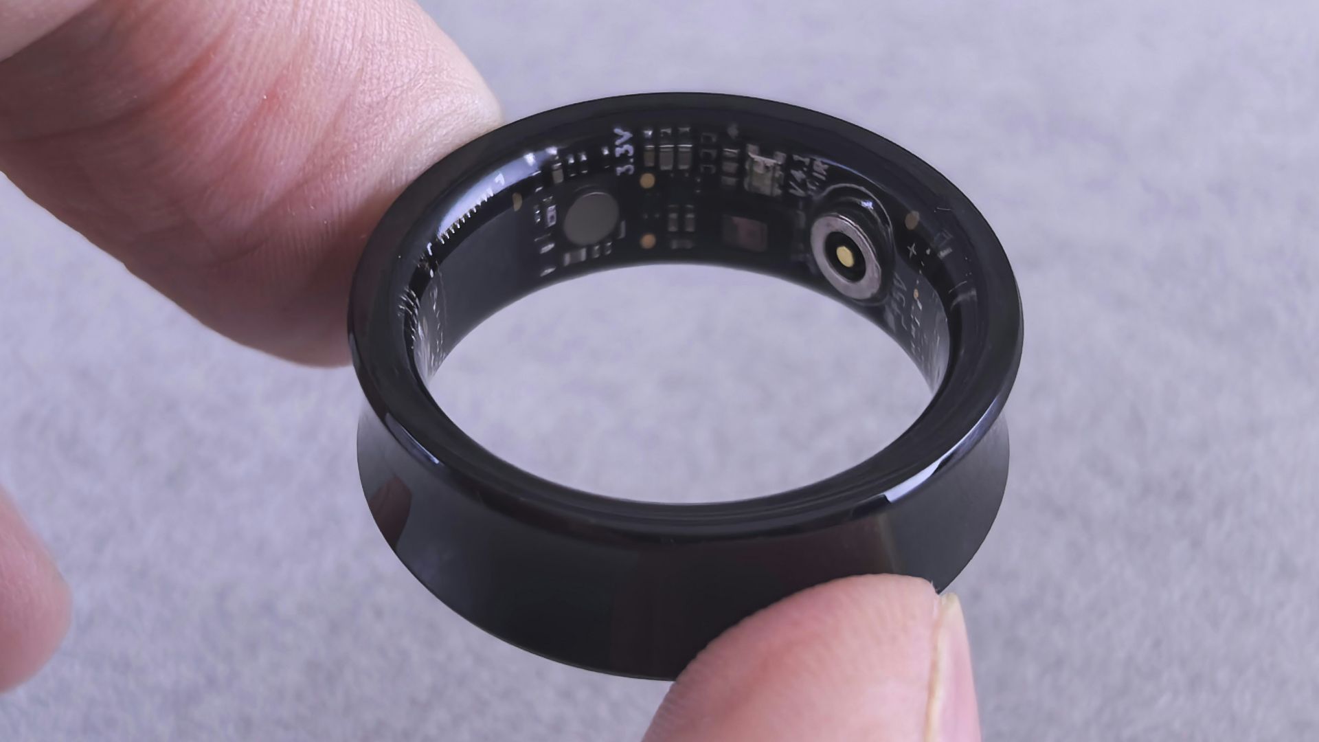 Fingers hold a black smart ring with circuits visible.