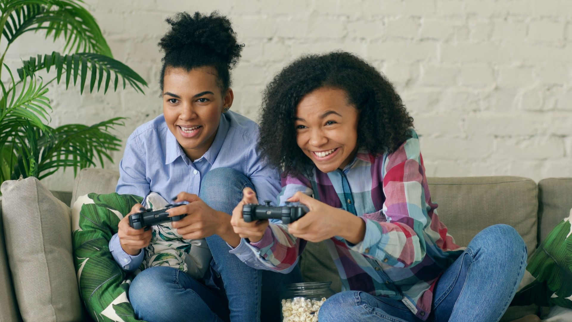 Two smiling girls playing video games on couch.