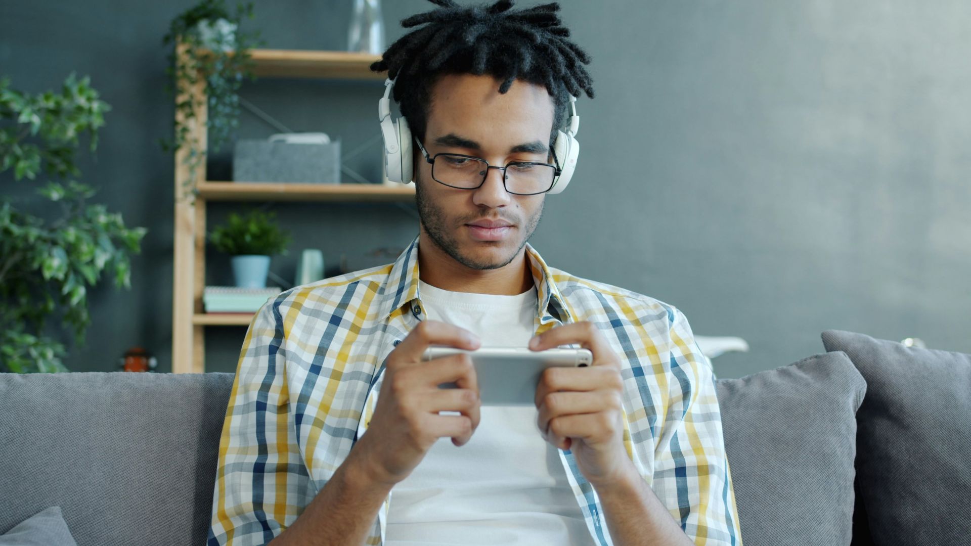 Man wearing headphones plays game on smartphone.