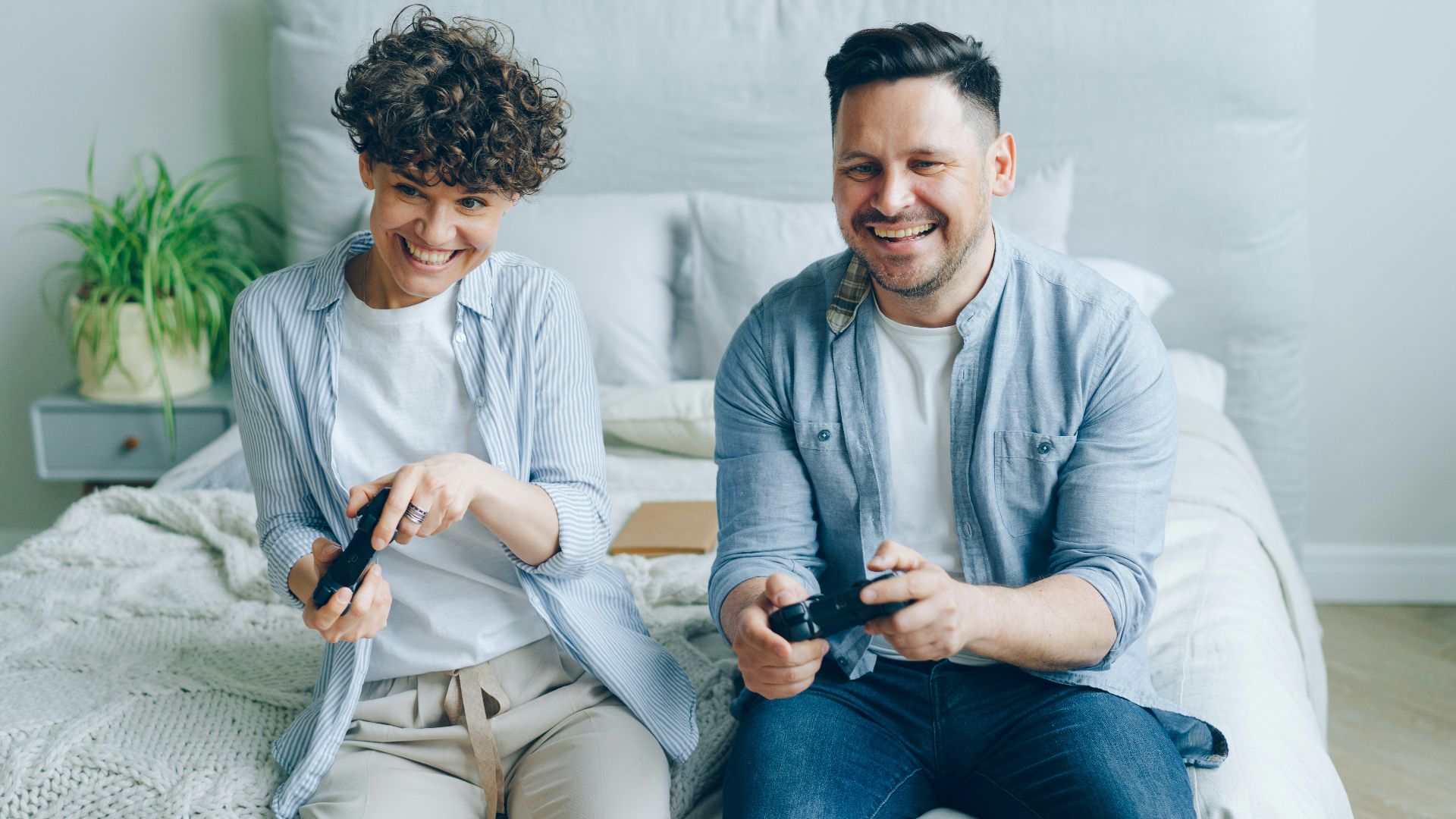 a man and a woman sitting on a bed playing a video game