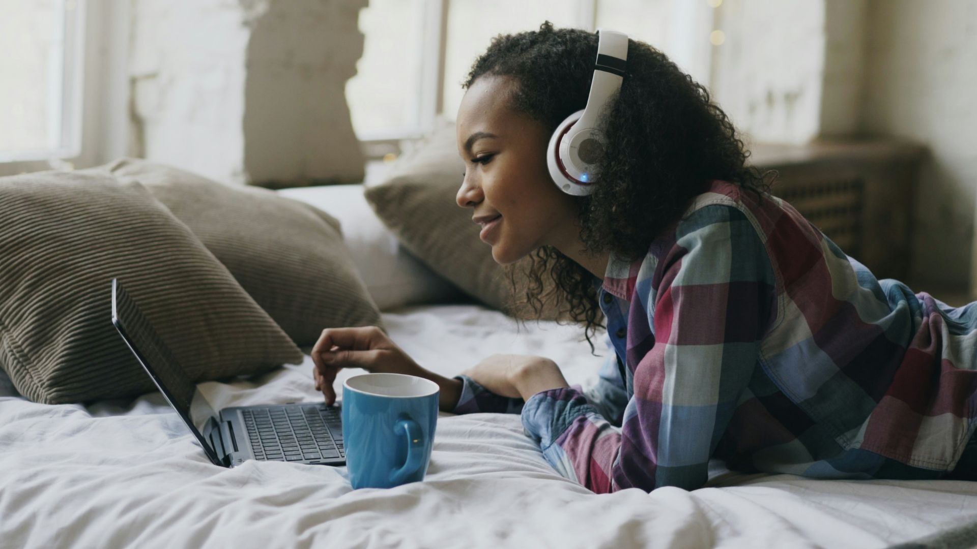 Young woman wearing headphones on bed with laptop.