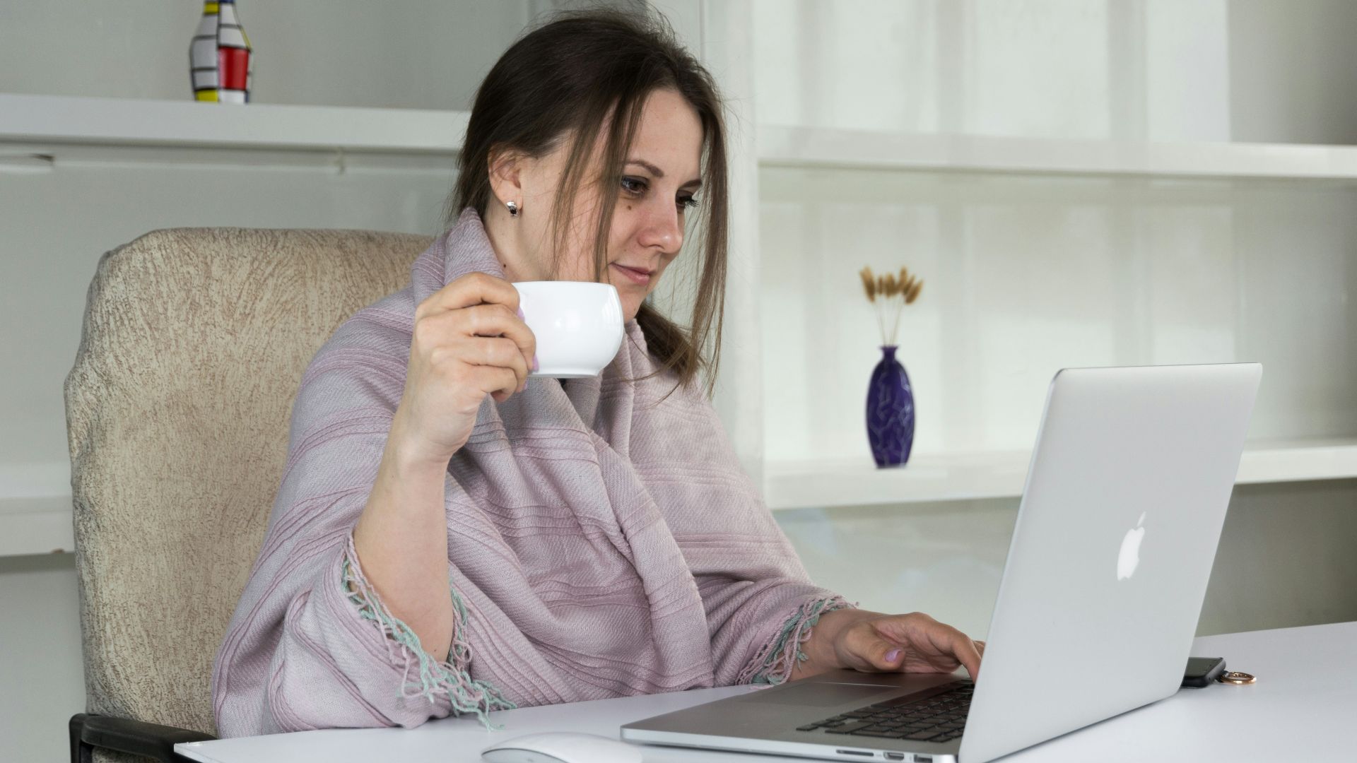 a woman sitting at a desk with a laptop and a cup of coffee