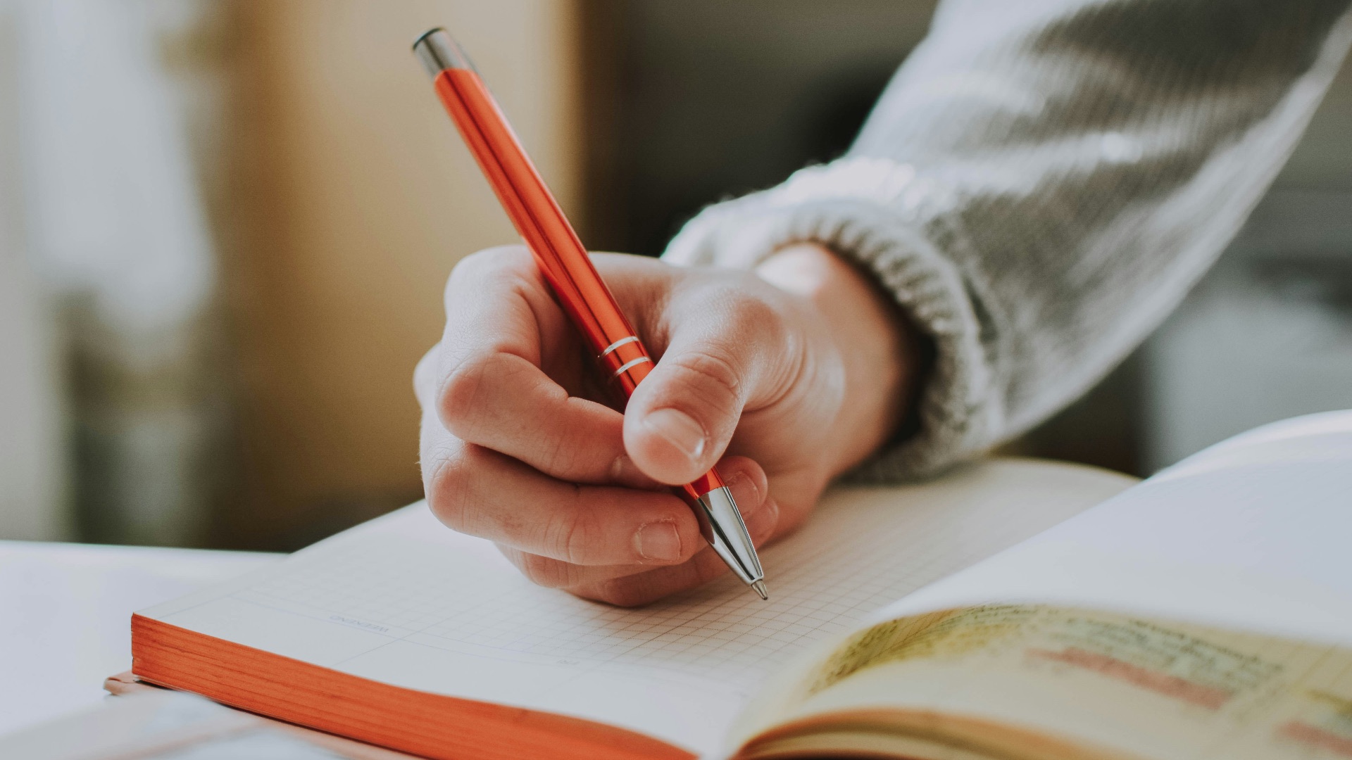 person holding on red pen while writing on book