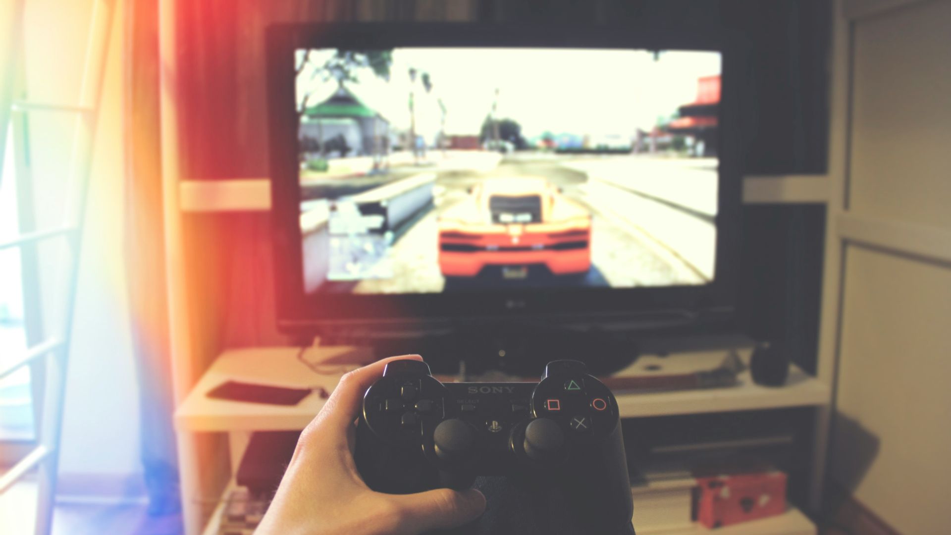 person holding Sony PS3 controller in front of flat screen monitor