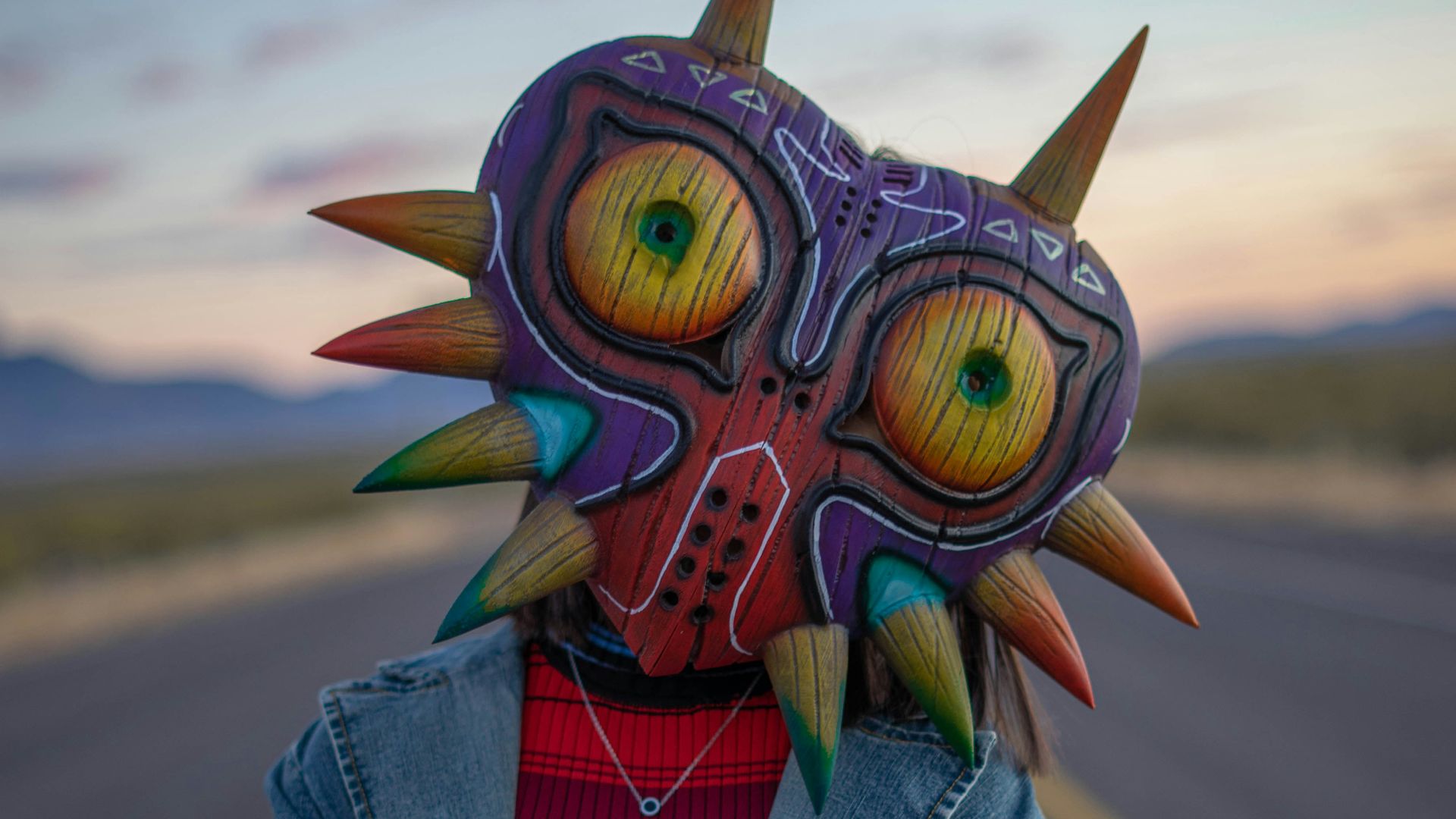 person in blue denim jacket with yellow green and blue owl mask
