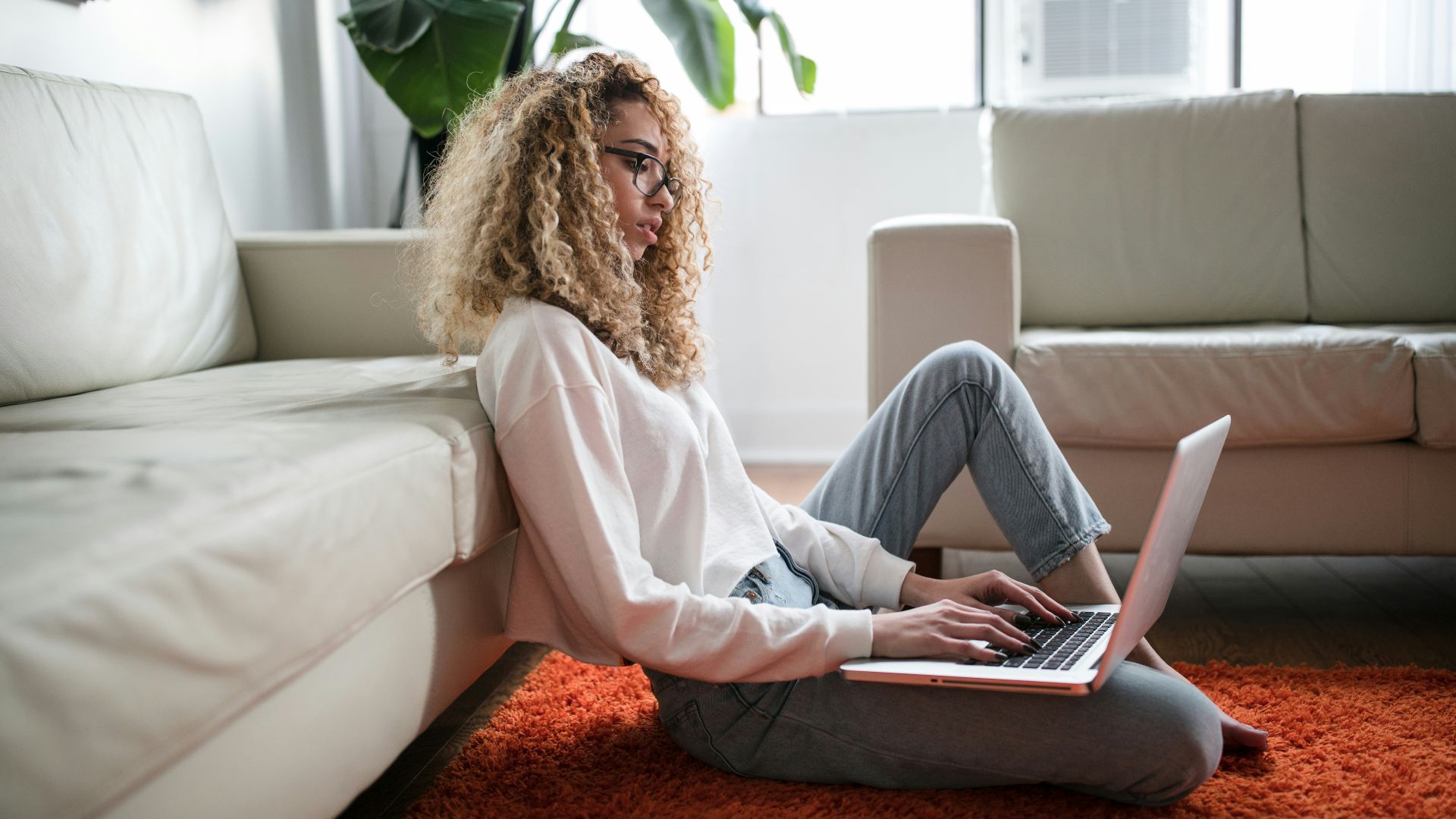 woman sitting on floor and leaning on couch using laptop