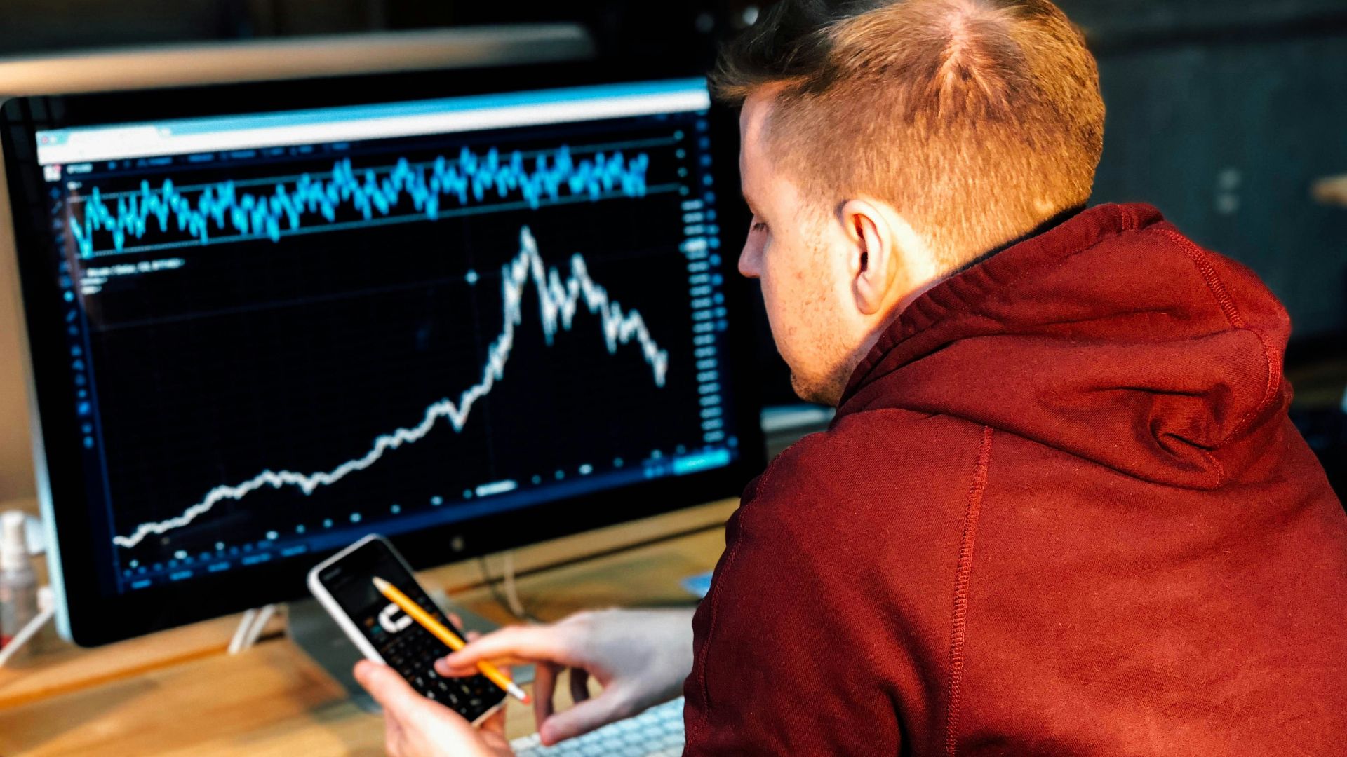 man holding black smartphone with flat screen monitor in front