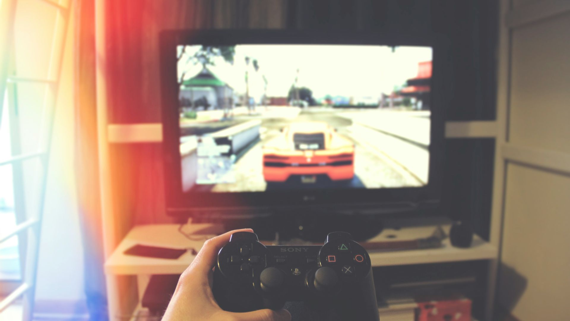 person holding Sony PS3 controller in front of flat screen monitor