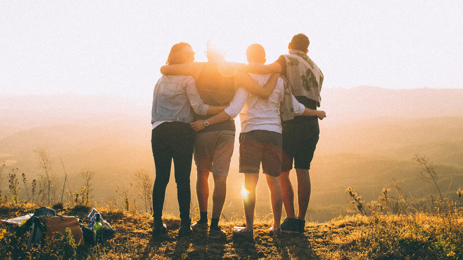 four person hands wrap around shoulders while looking at sunset
