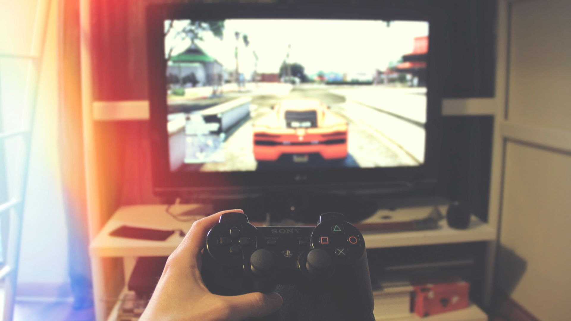 person holding Sony PS3 controller in front of flat screen monitor