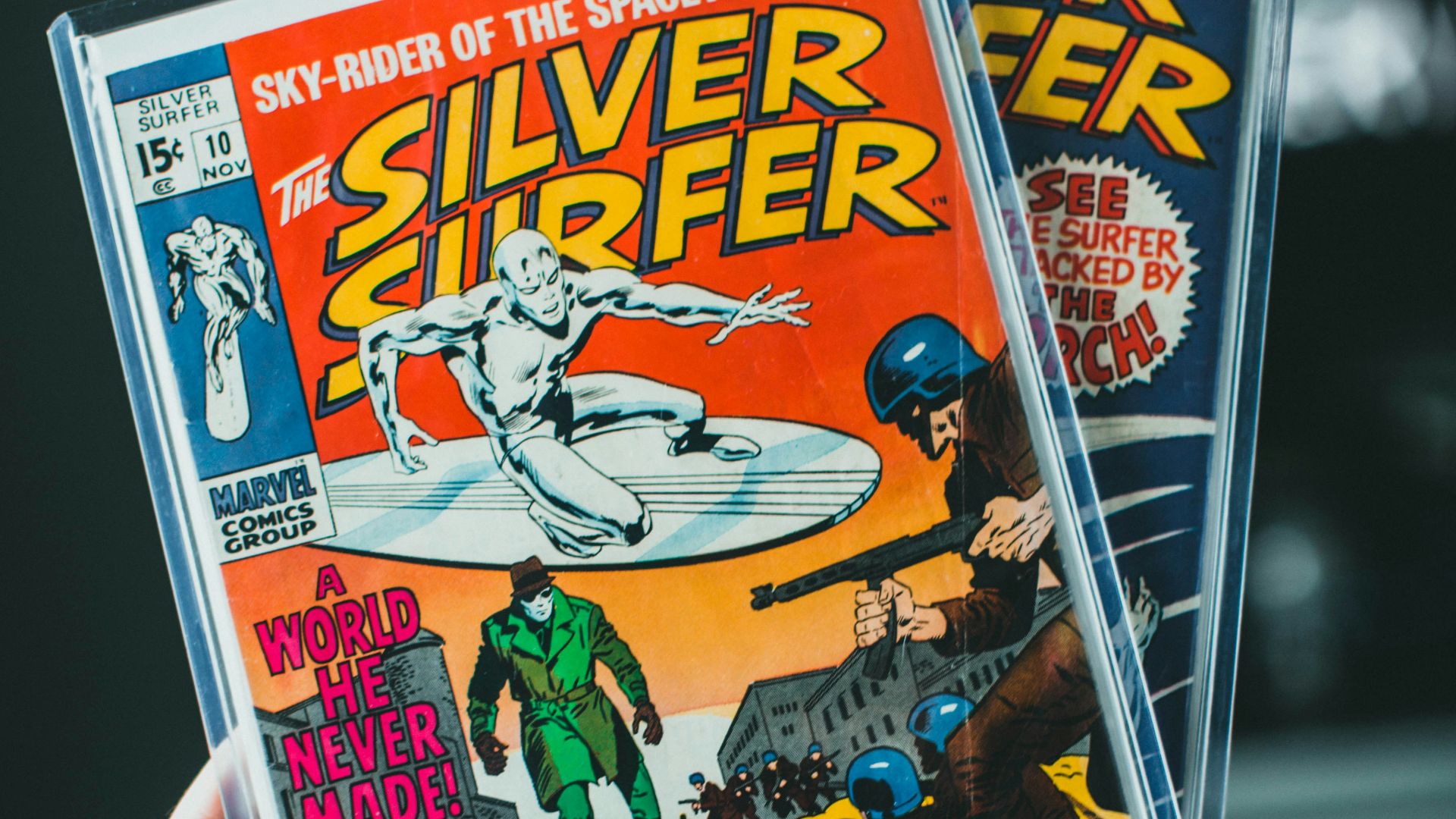 a person holding up two silver surfer comics