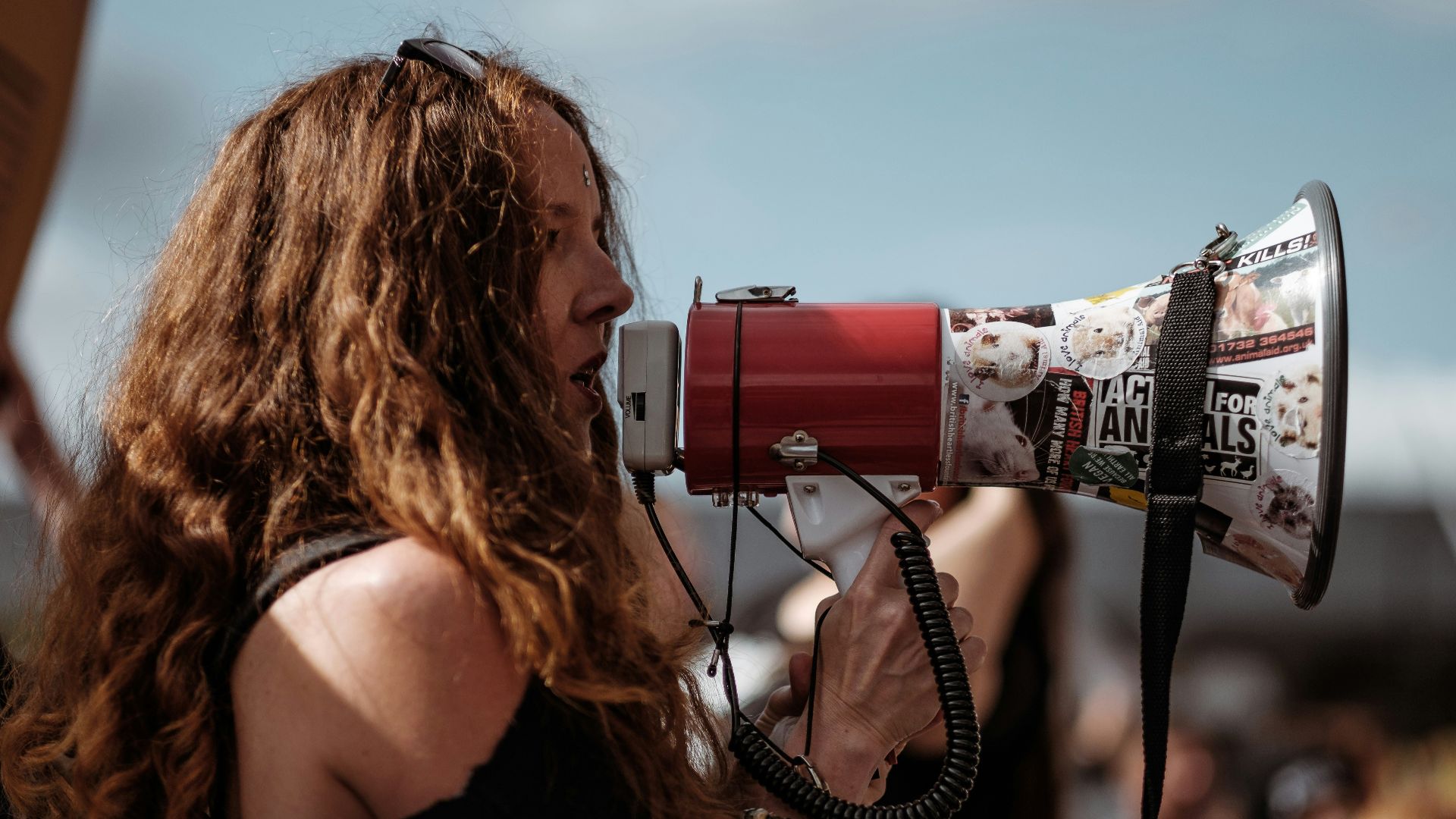 selective focus photography of woman wearing black cold-shoulder shirt using megaphone during daytime