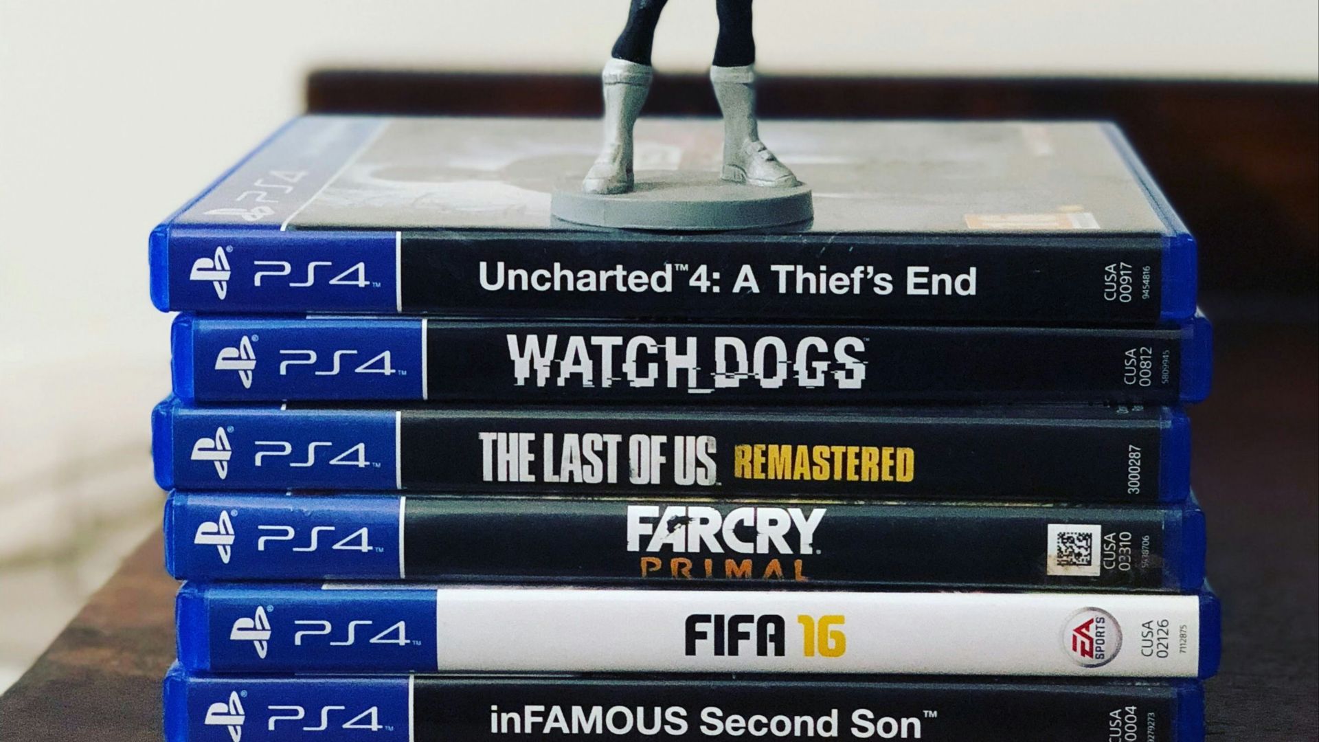 assorted-title Sony PS4 game cases with figurine on top