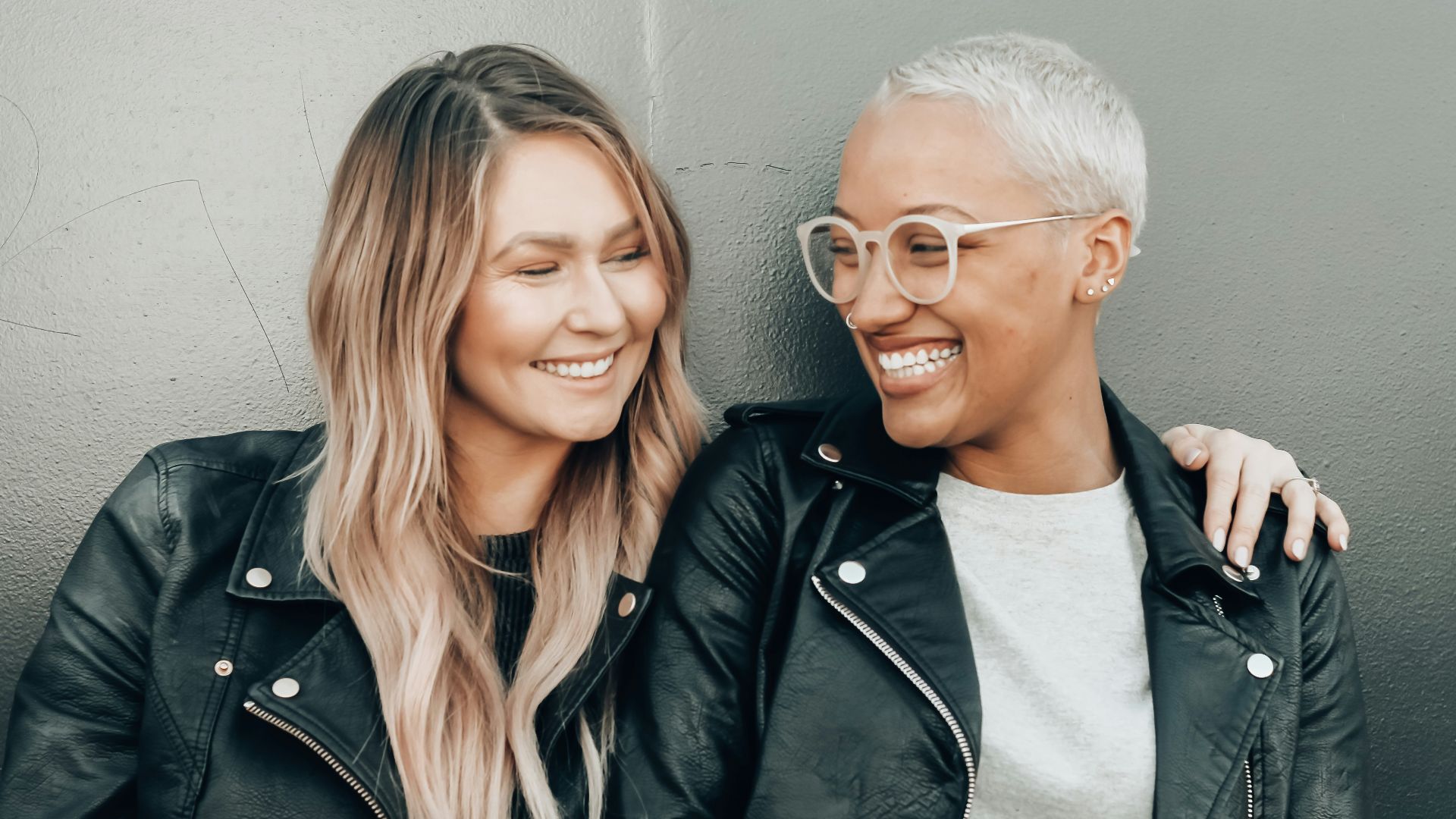 woman in black leather jacket beside woman in gray shirt