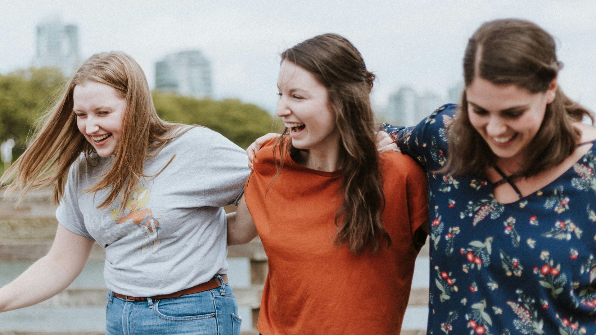 three women walking on brown wooden dock near high rise building during daytime