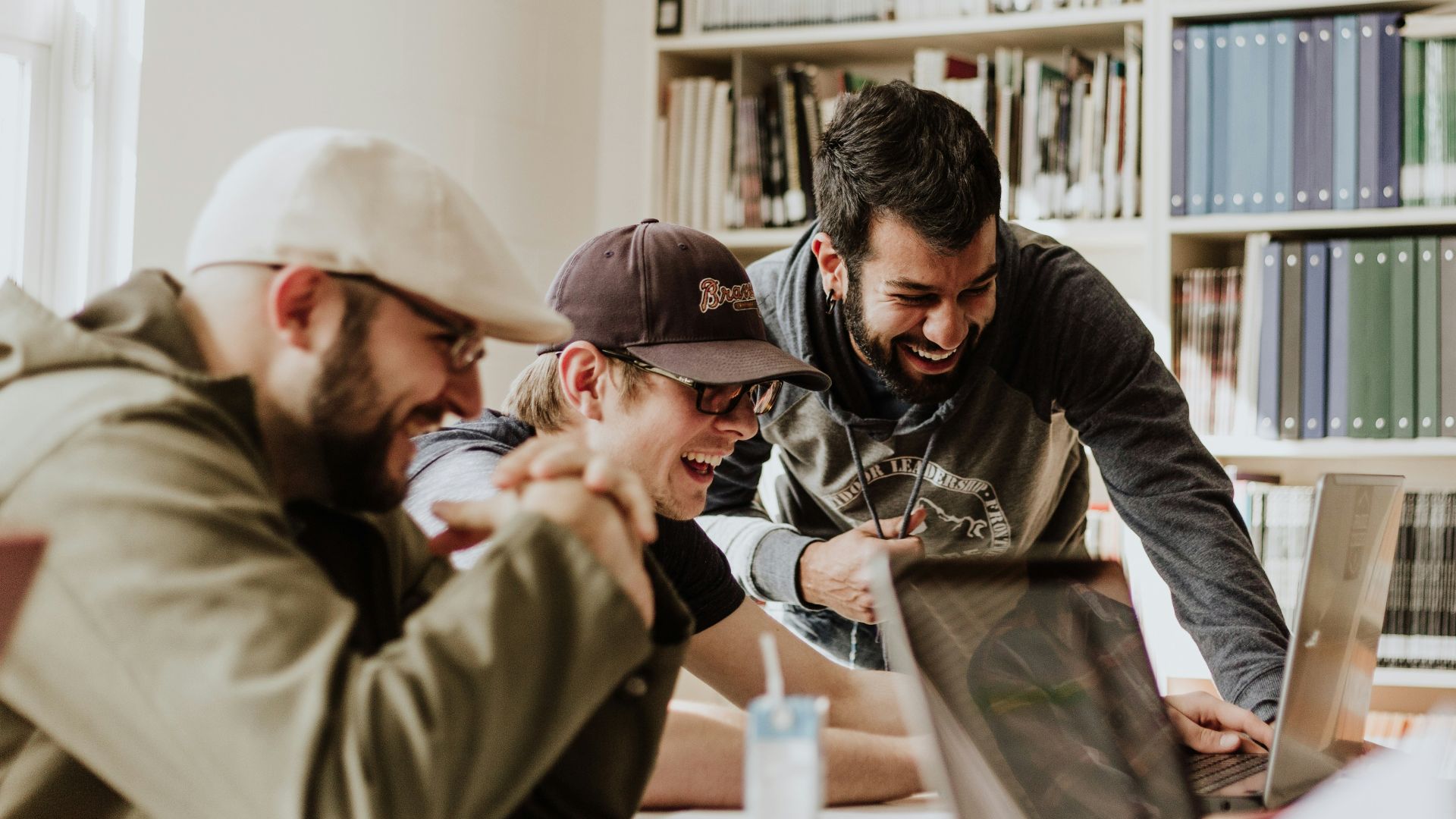three men laughing while looking in the laptop inside room