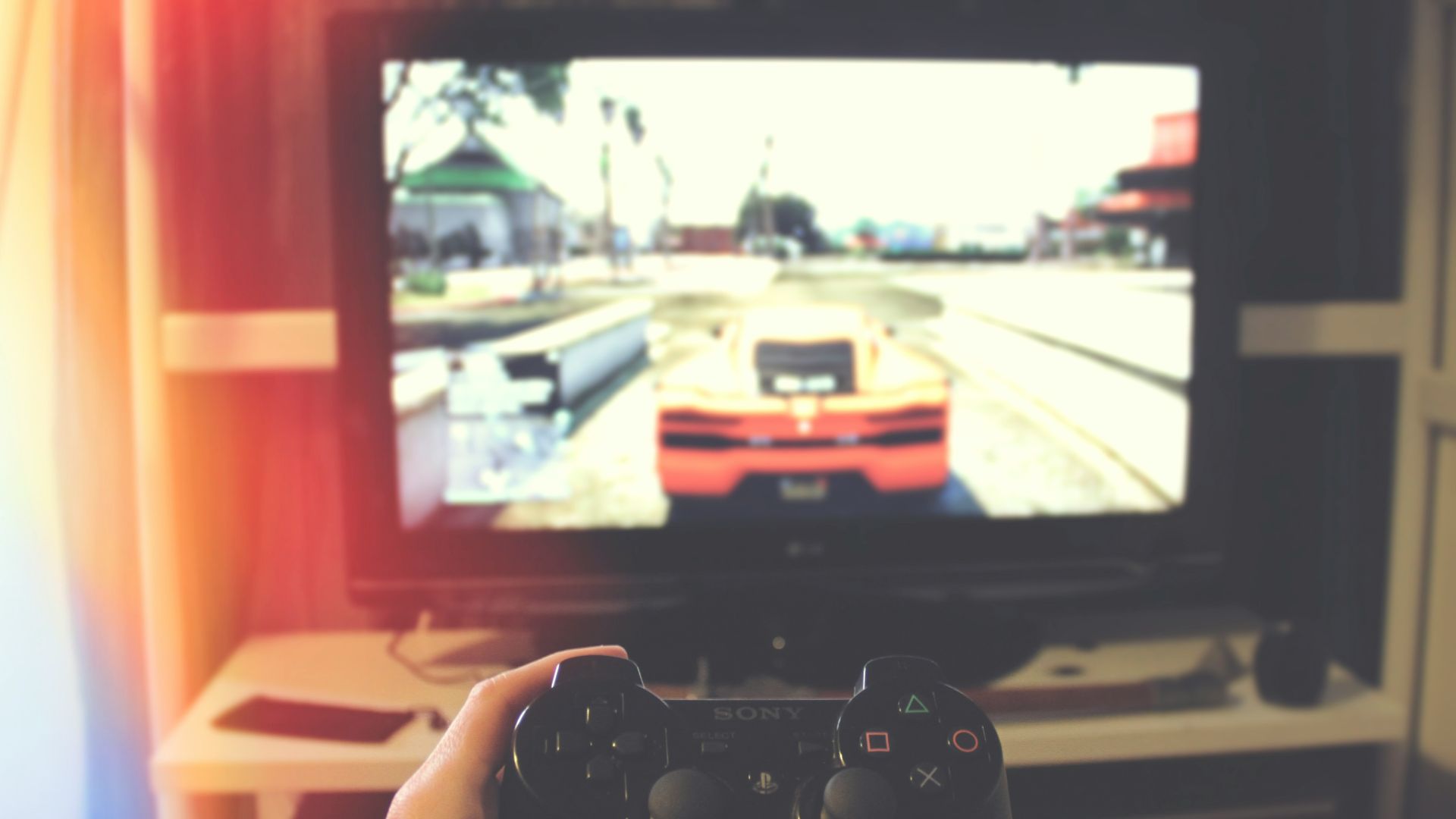 person holding Sony PS3 controller in front of flat screen monitor