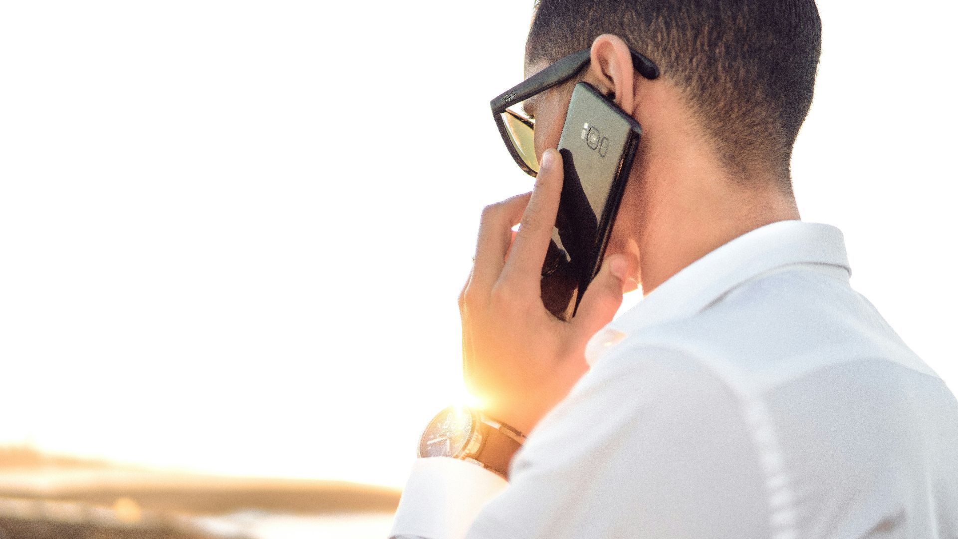 man holding smartphone standing in front of calm body of water