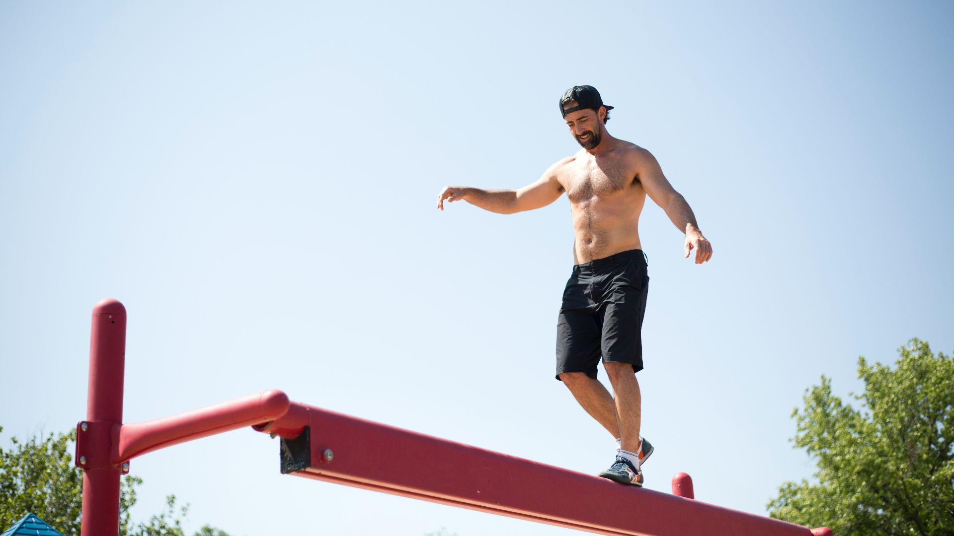 man wearing black shorts walking on red metal beam