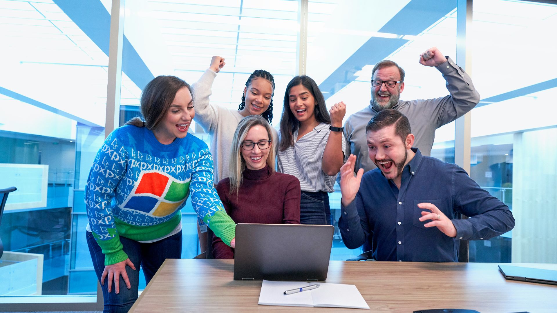 men and women sitting and standing by the table looking happy while staring at laptop