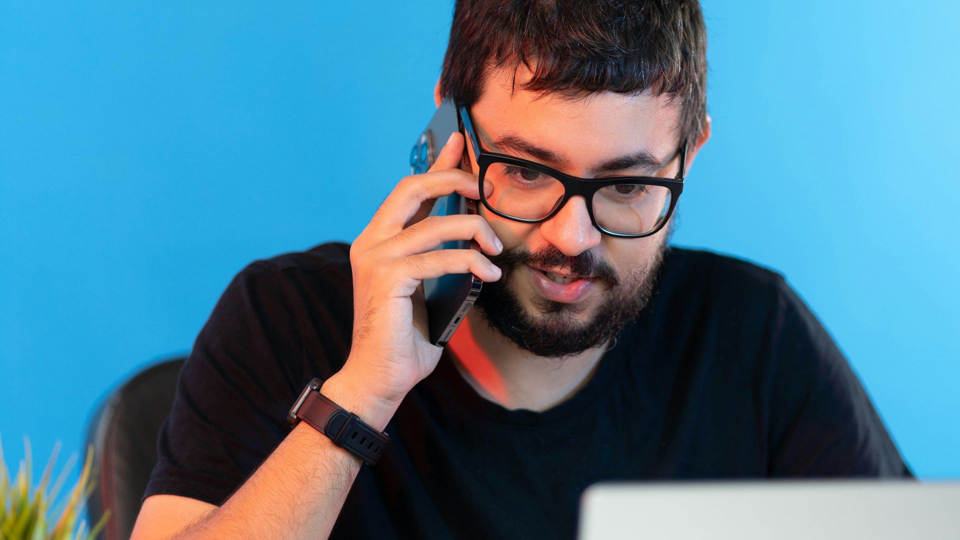 a man sitting in front of a laptop talking on a cell phone