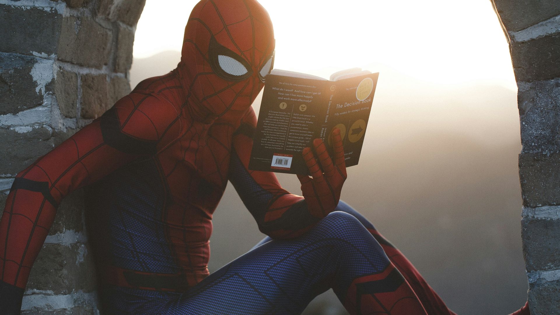 Spider-Man leaning on concrete brick while reading book