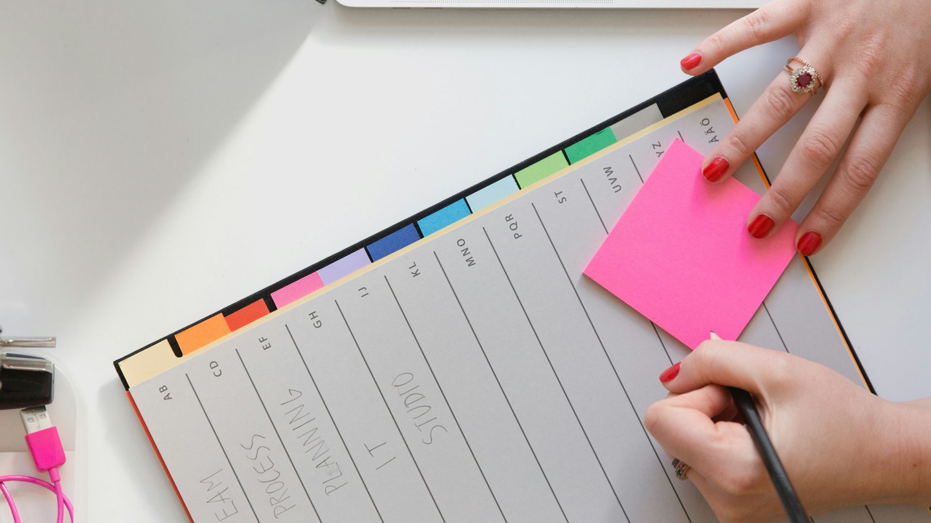person holding pencil and stick note beside table