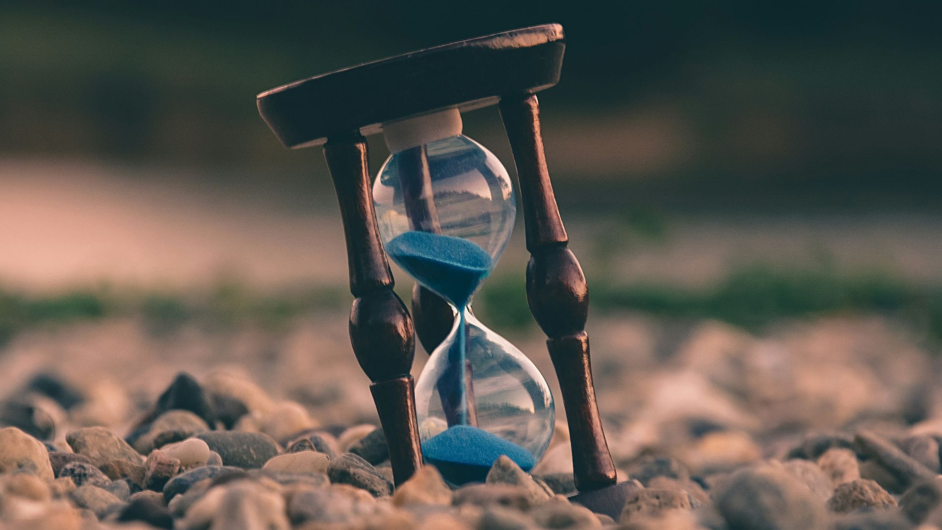 selective focus photo of brown and blue hourglass on stones