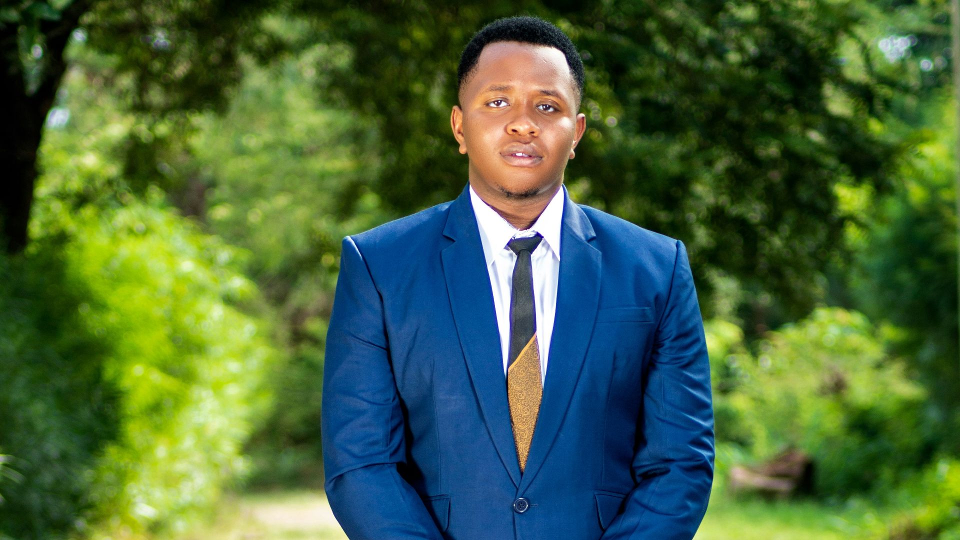 A man in a blue suit poses outdoors.