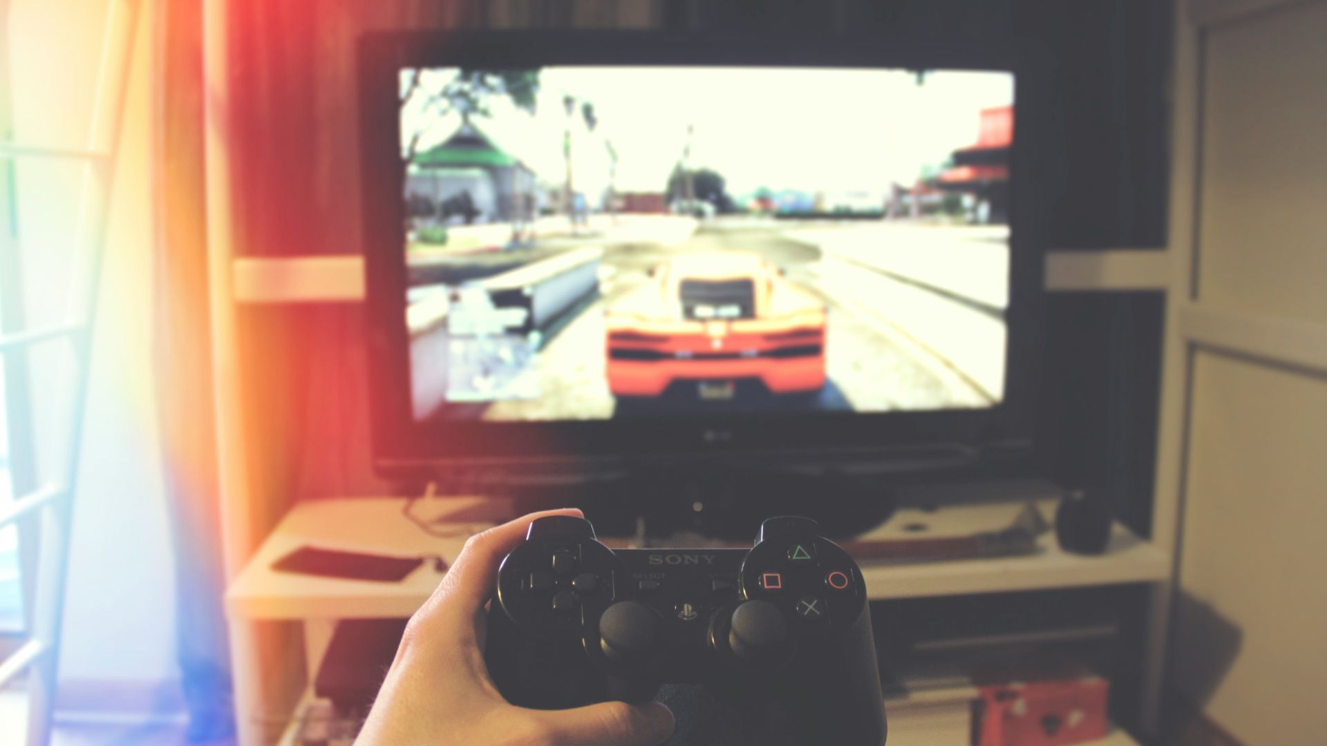 person holding Sony PS3 controller in front of flat screen monitor