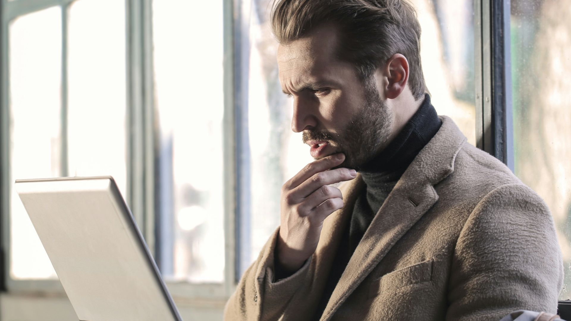 man holding his chin facing laptop computer