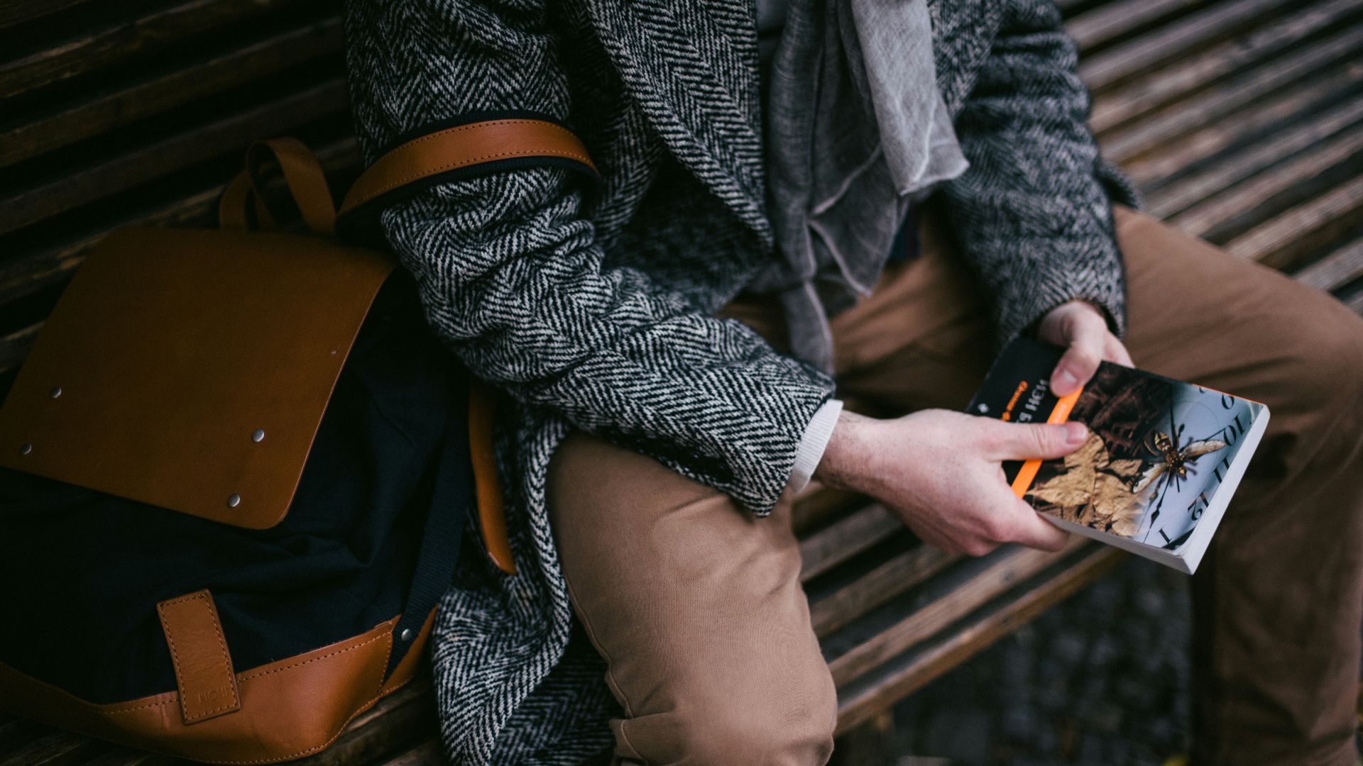 A person reads a book while sitting on a bench.