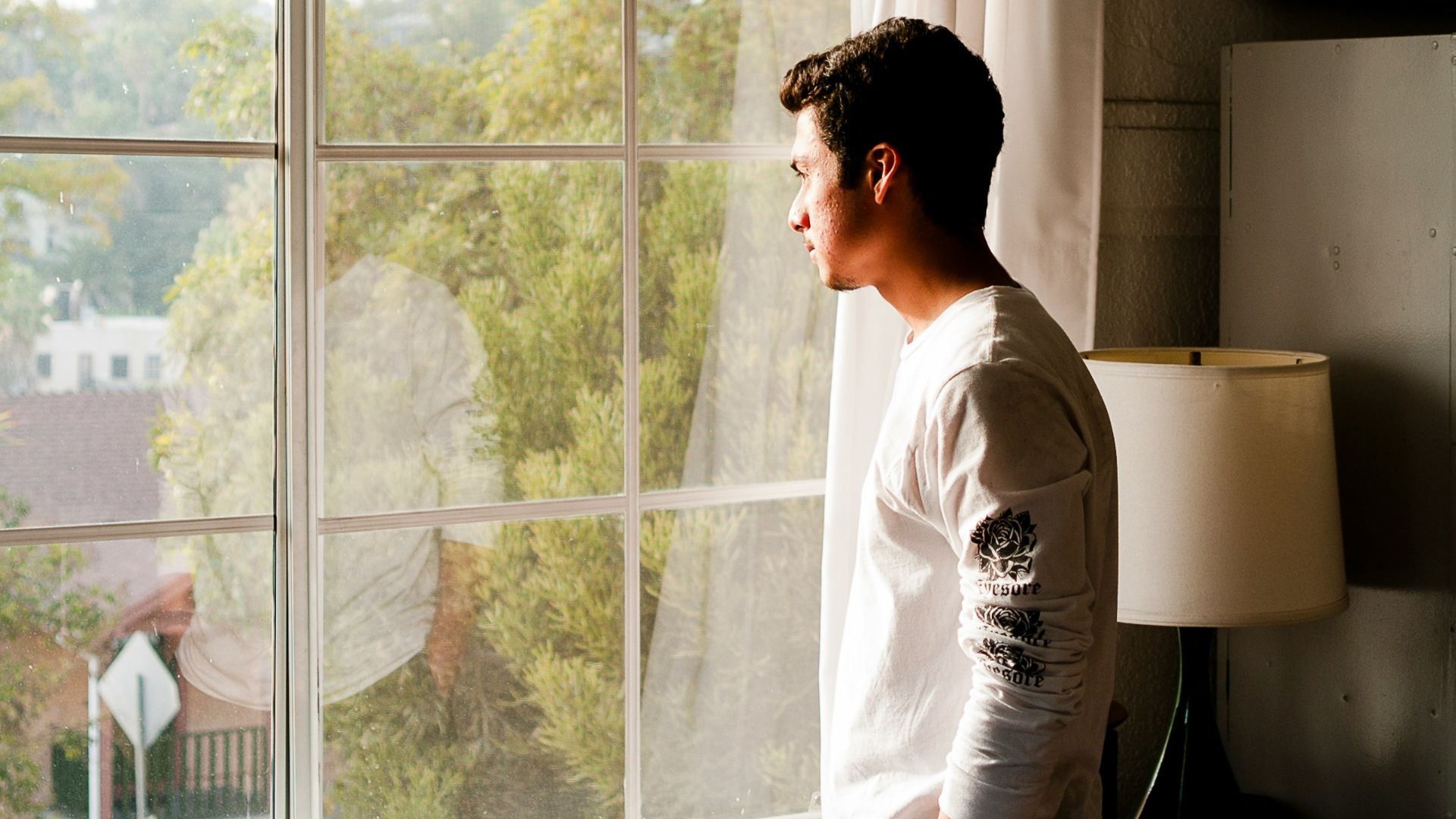 man wearing gray and black crew-neck shirt standing and looking out window