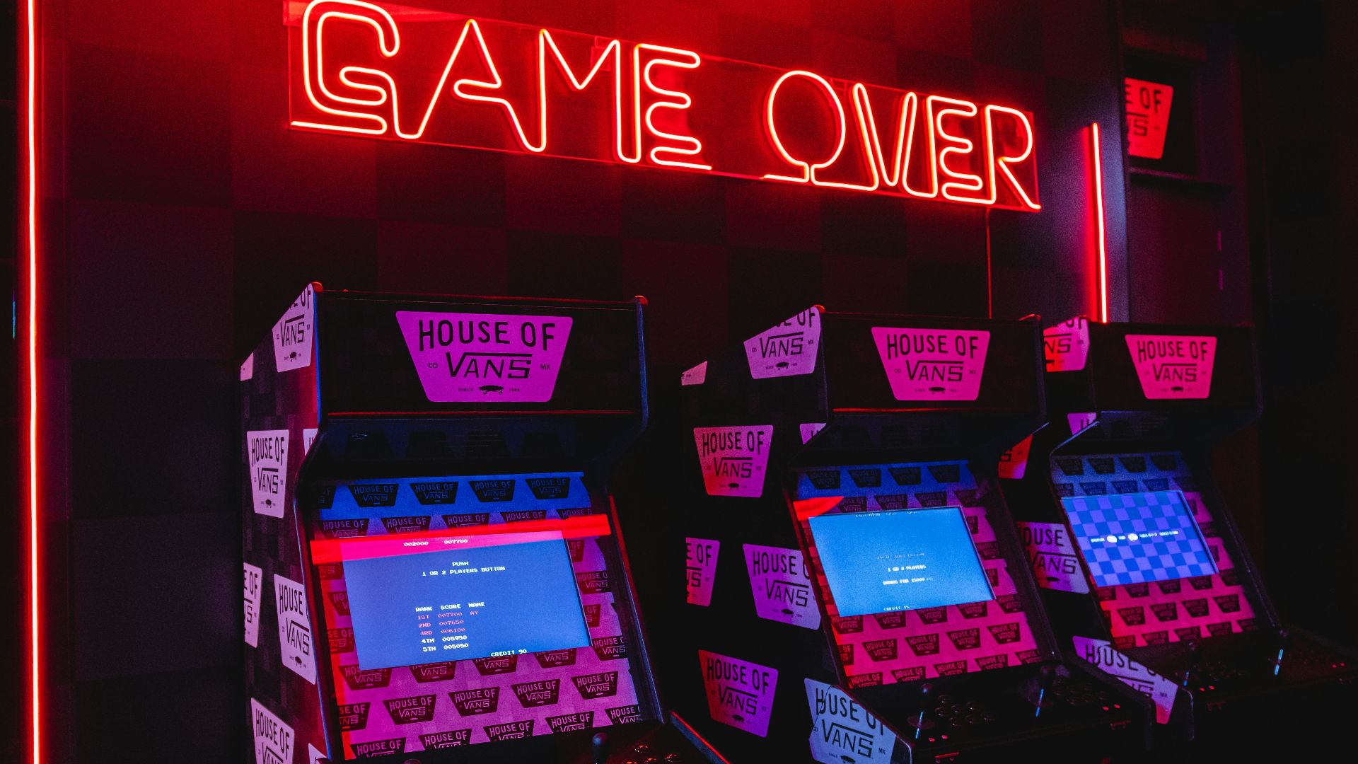 a neon sign that says game over in front of a row of arcade machines