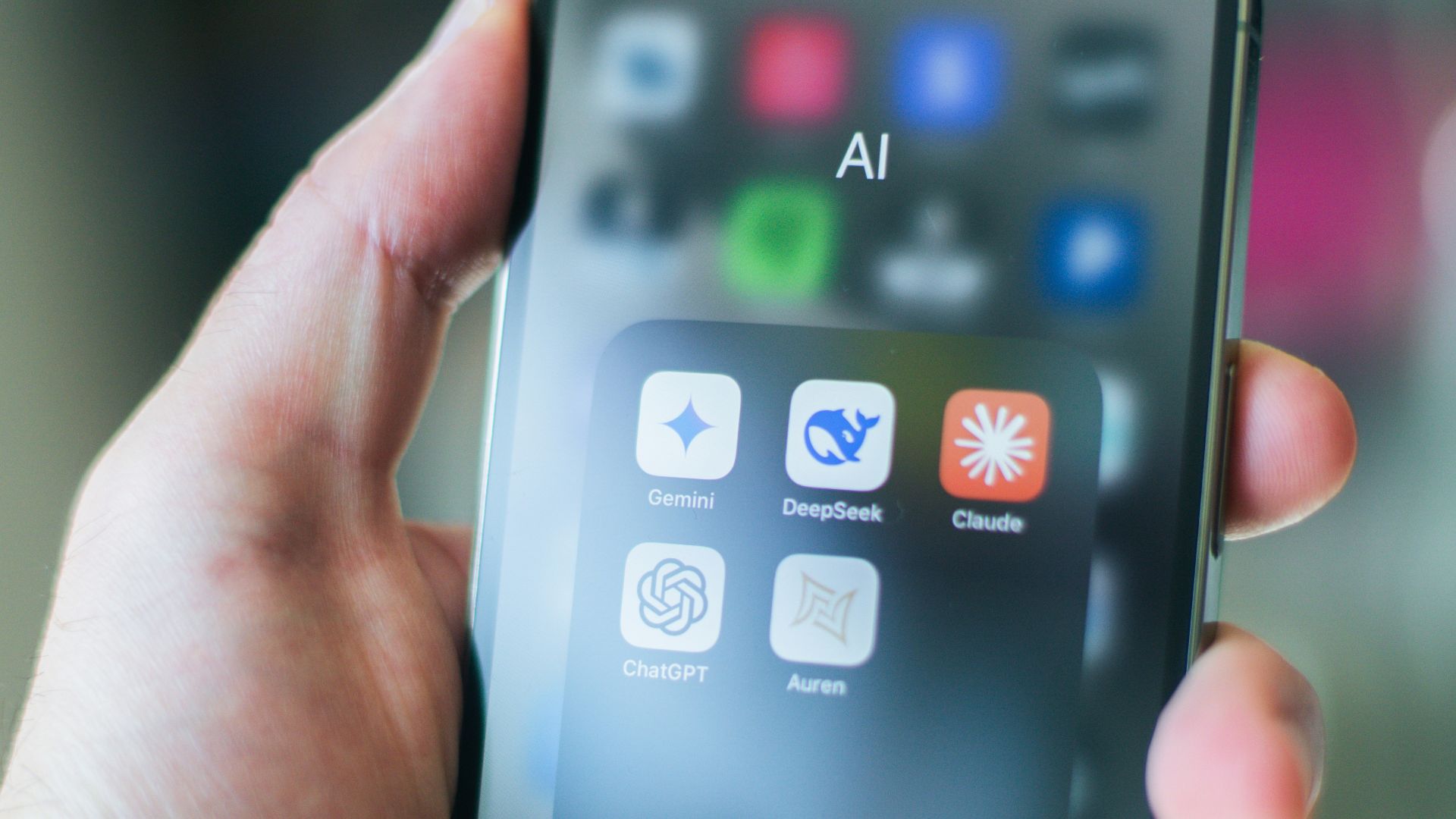 A hand holds a smartphone with various apps.