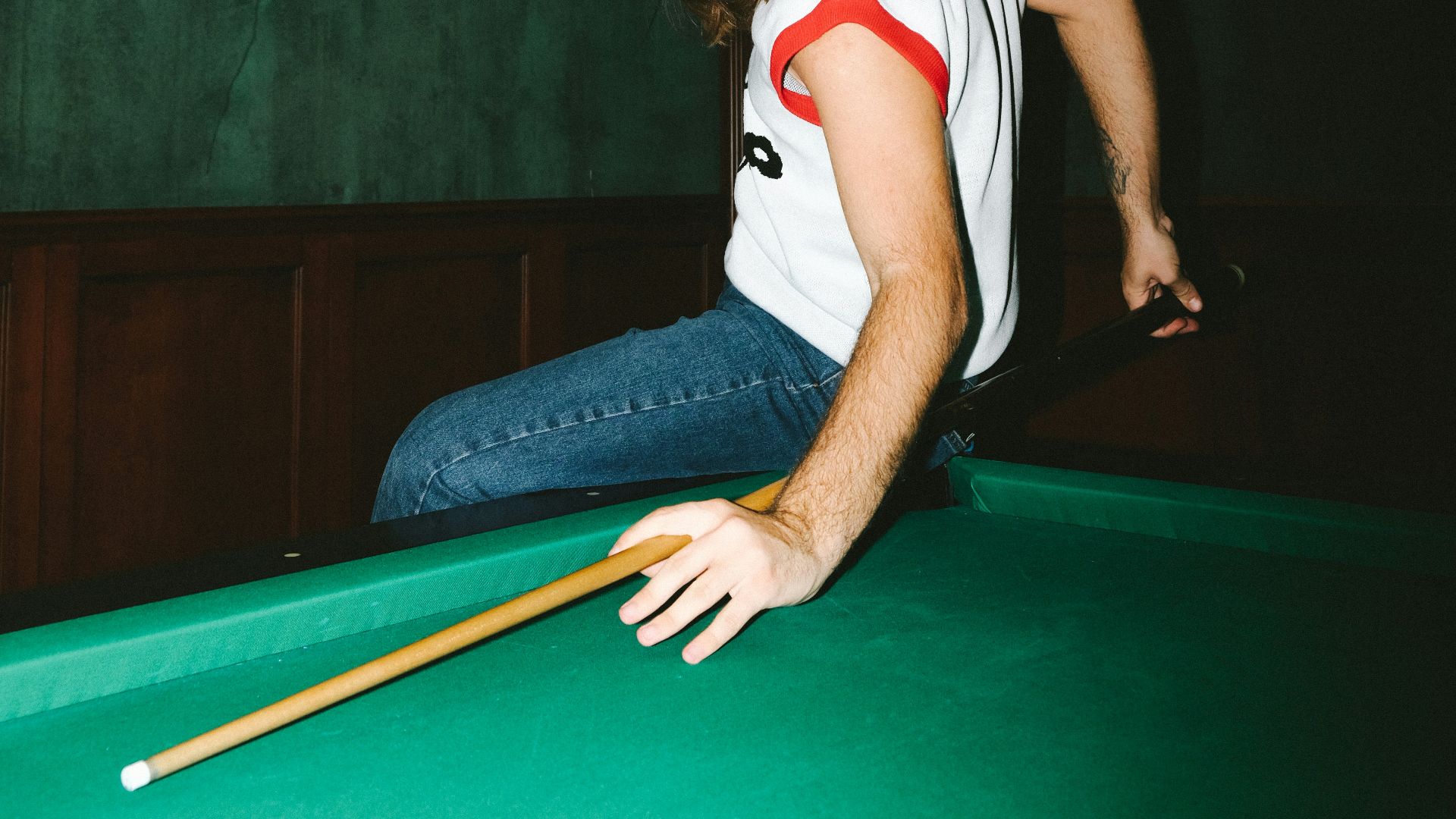 woman in white and red jersey shirt and blue denim jeans sitting on billiard table