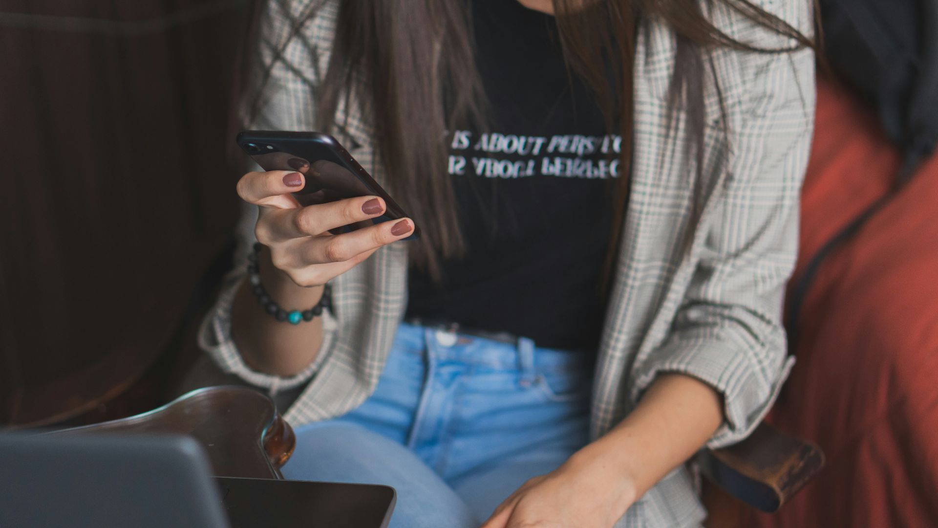 woman in white cardigan holding black smartphone