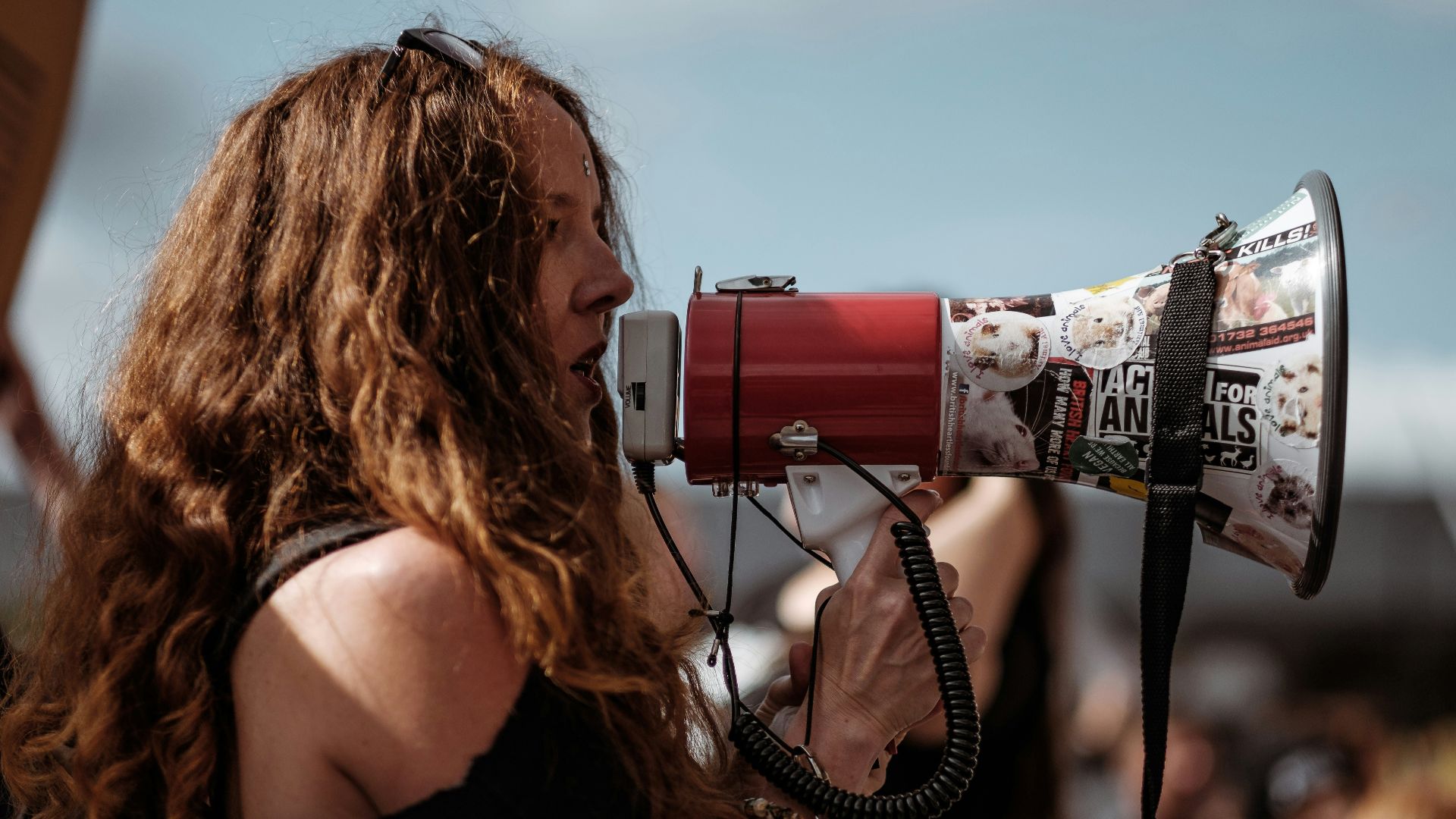 selective focus photography of woman wearing black cold-shoulder shirt using megaphone during daytime