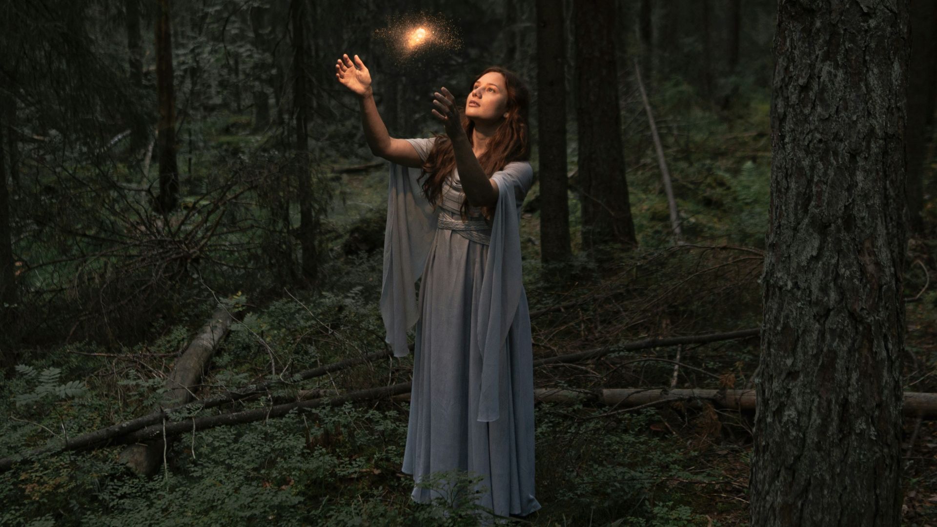 a woman standing in a forest holding a light in her hand