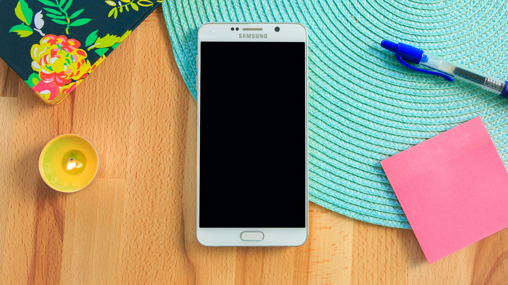 white Samsung Galaxy smartphone on top of blue place mat near blue click pen