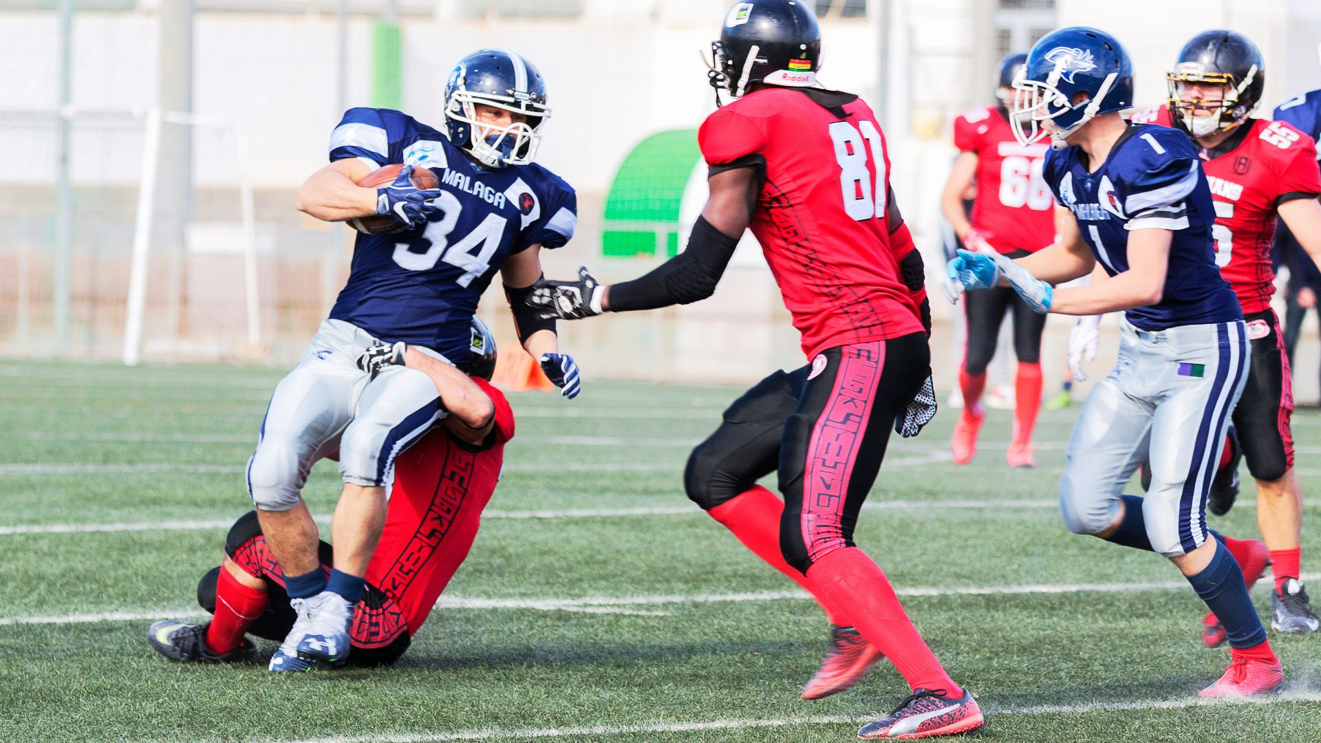 football players in red jersey shirt and red pants running on green grass field during daytime