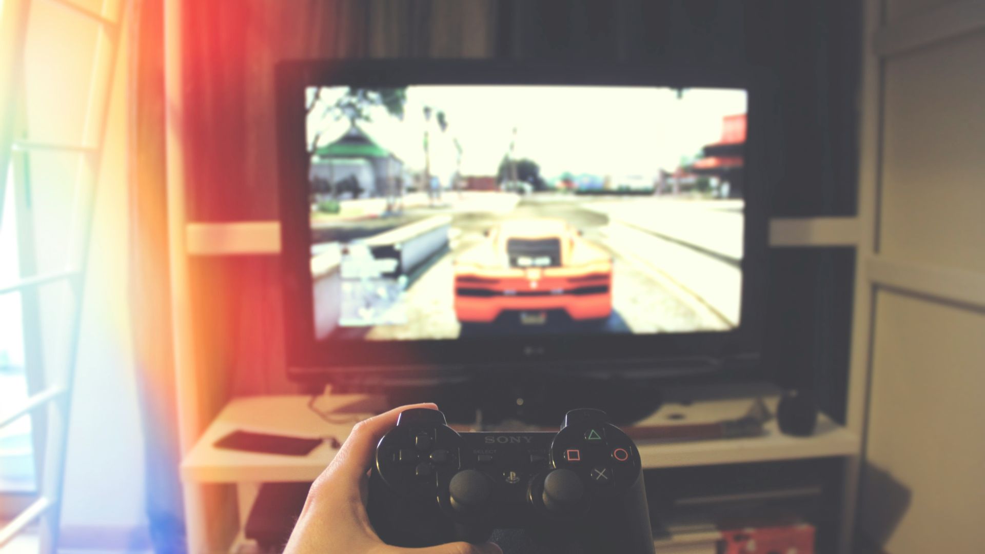 person holding Sony PS3 controller in front of flat screen monitor